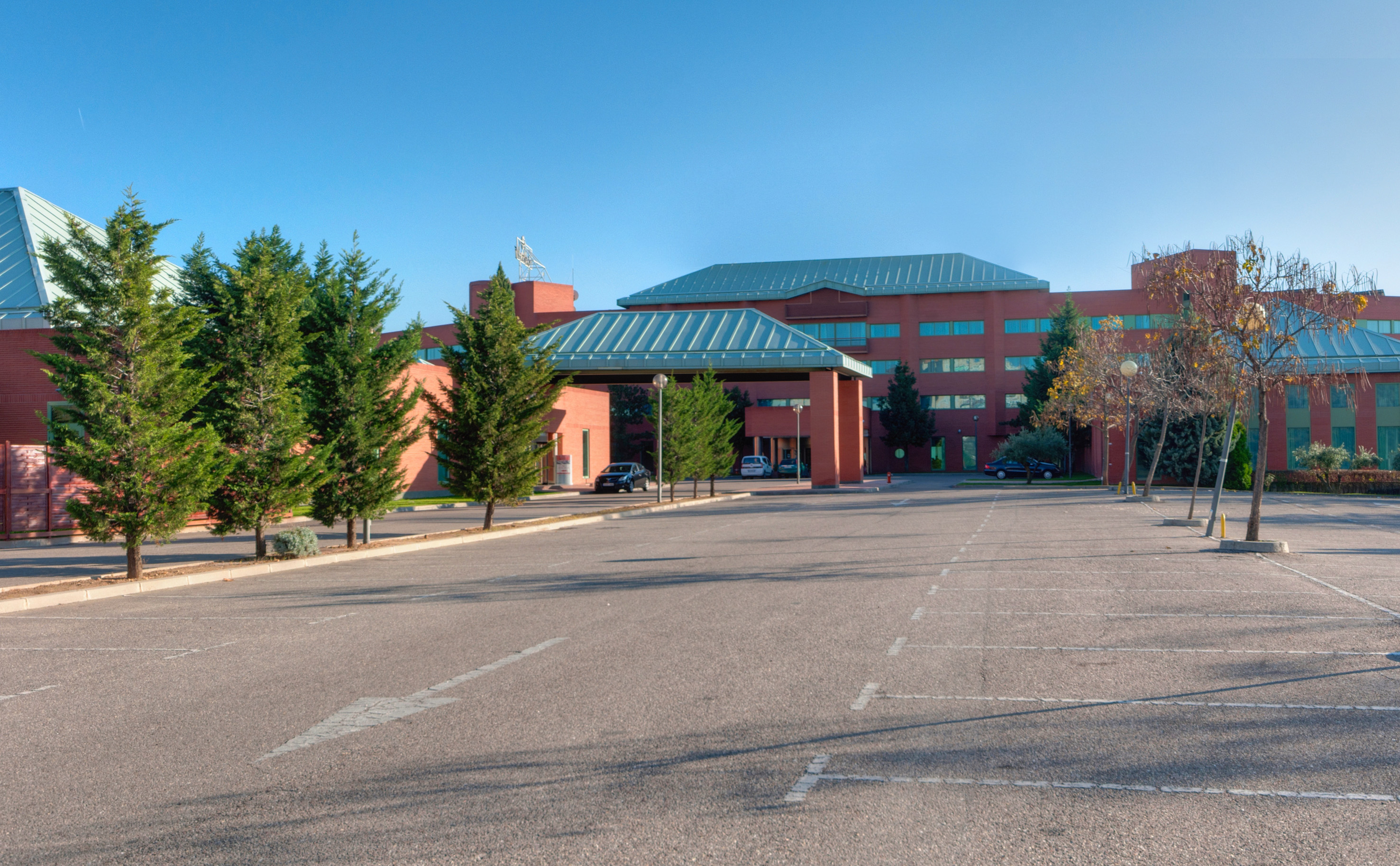 Red brick building, covered entry, empty parking lot, and green trees.