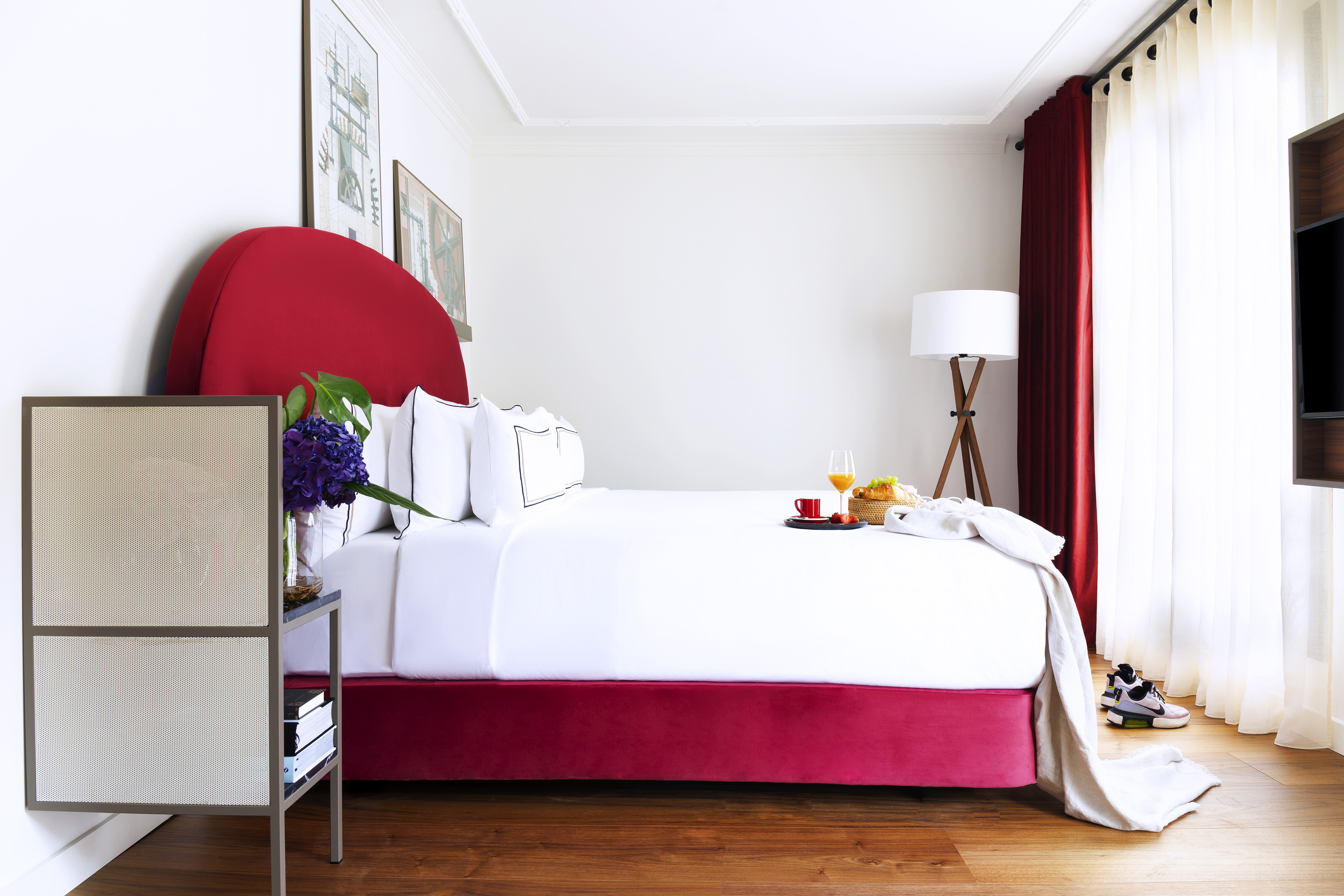 Modern hotel bedroom with red bed, white linens, and breakfast in bed tray.
