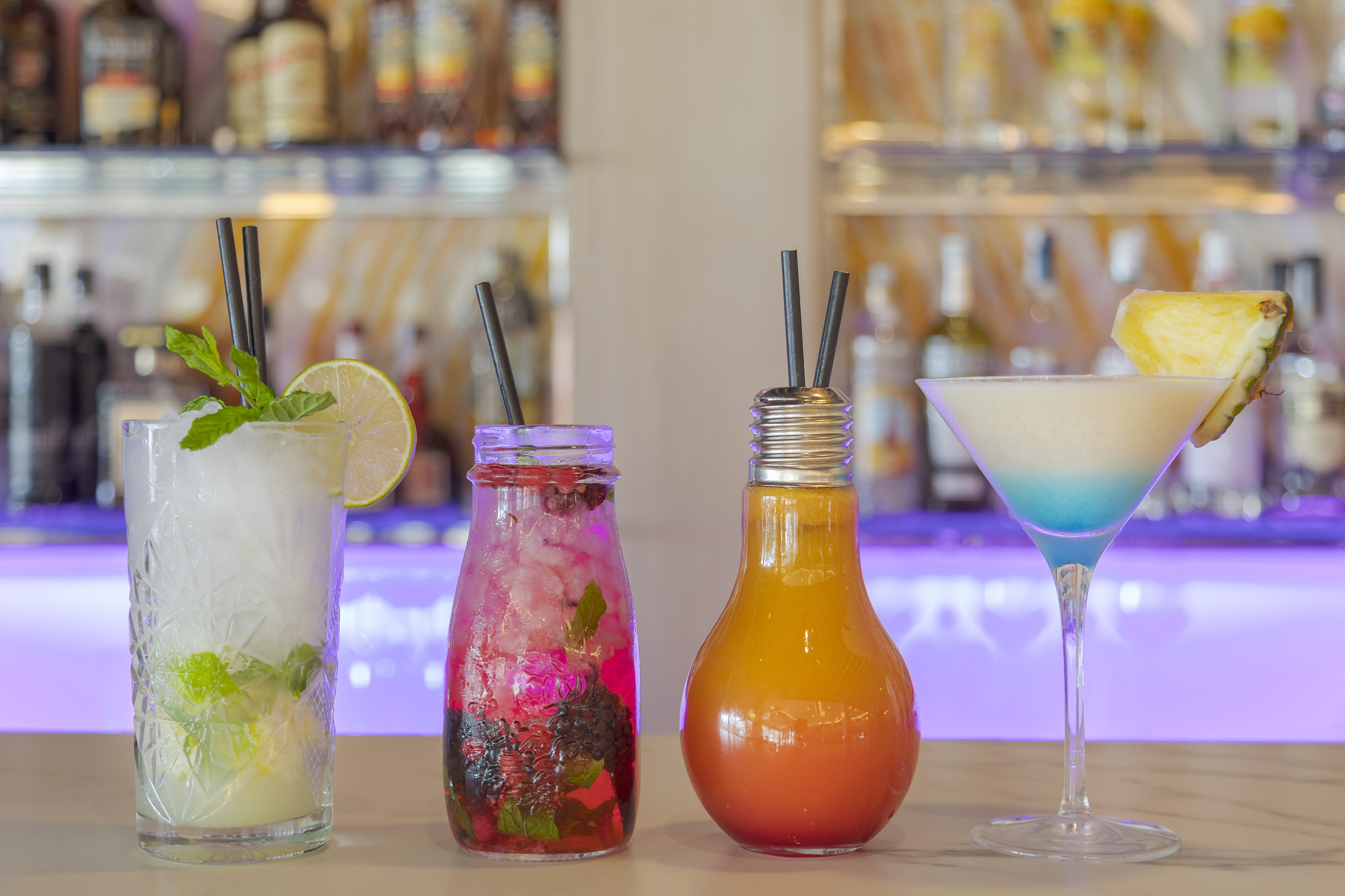 Vibrant bar cocktails: mojito, berry, pineapple, and lightbulb drinks on counter.