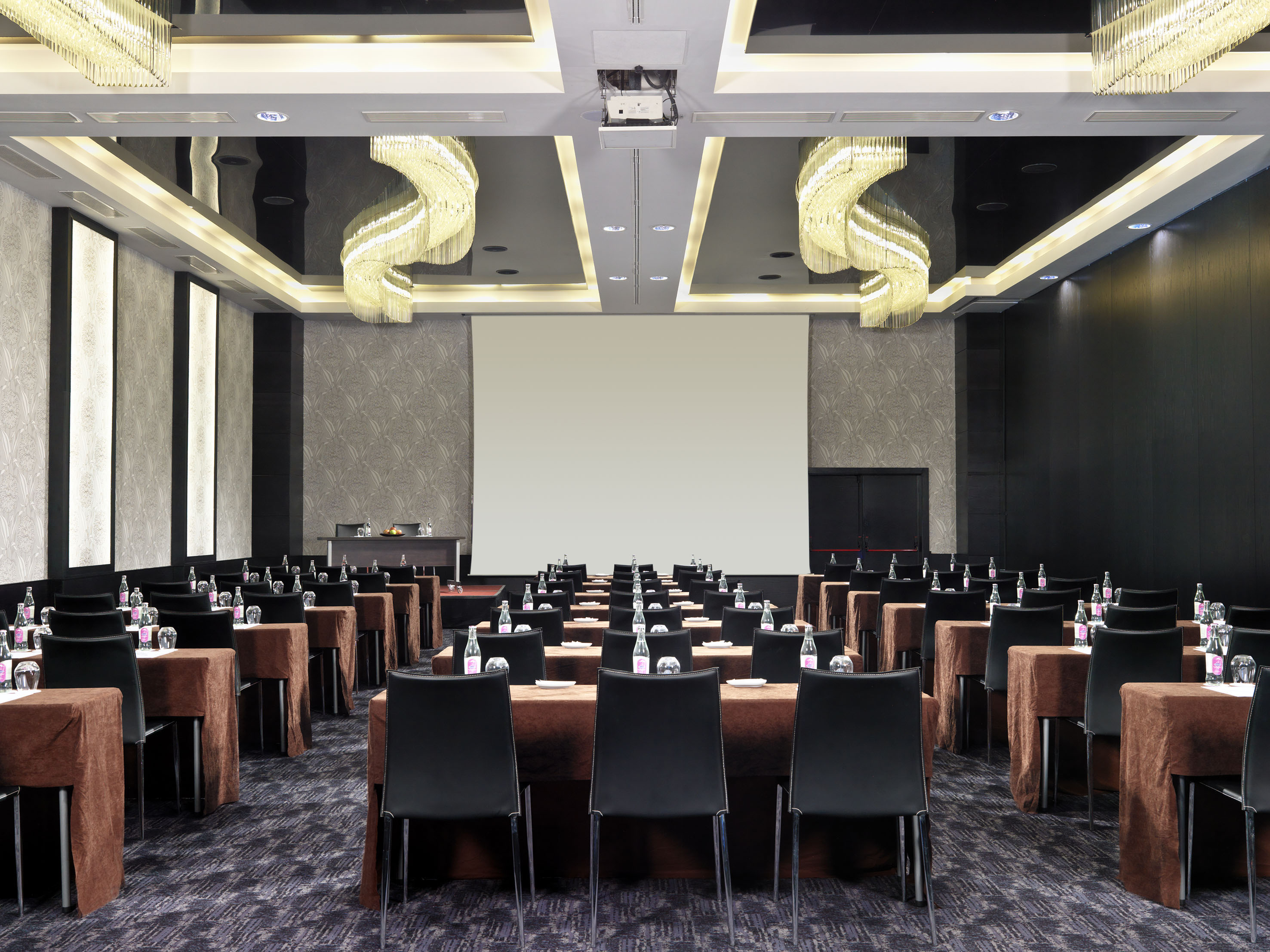 Elegant conference room with brown tables, black chairs, large screen, and chandeliers.