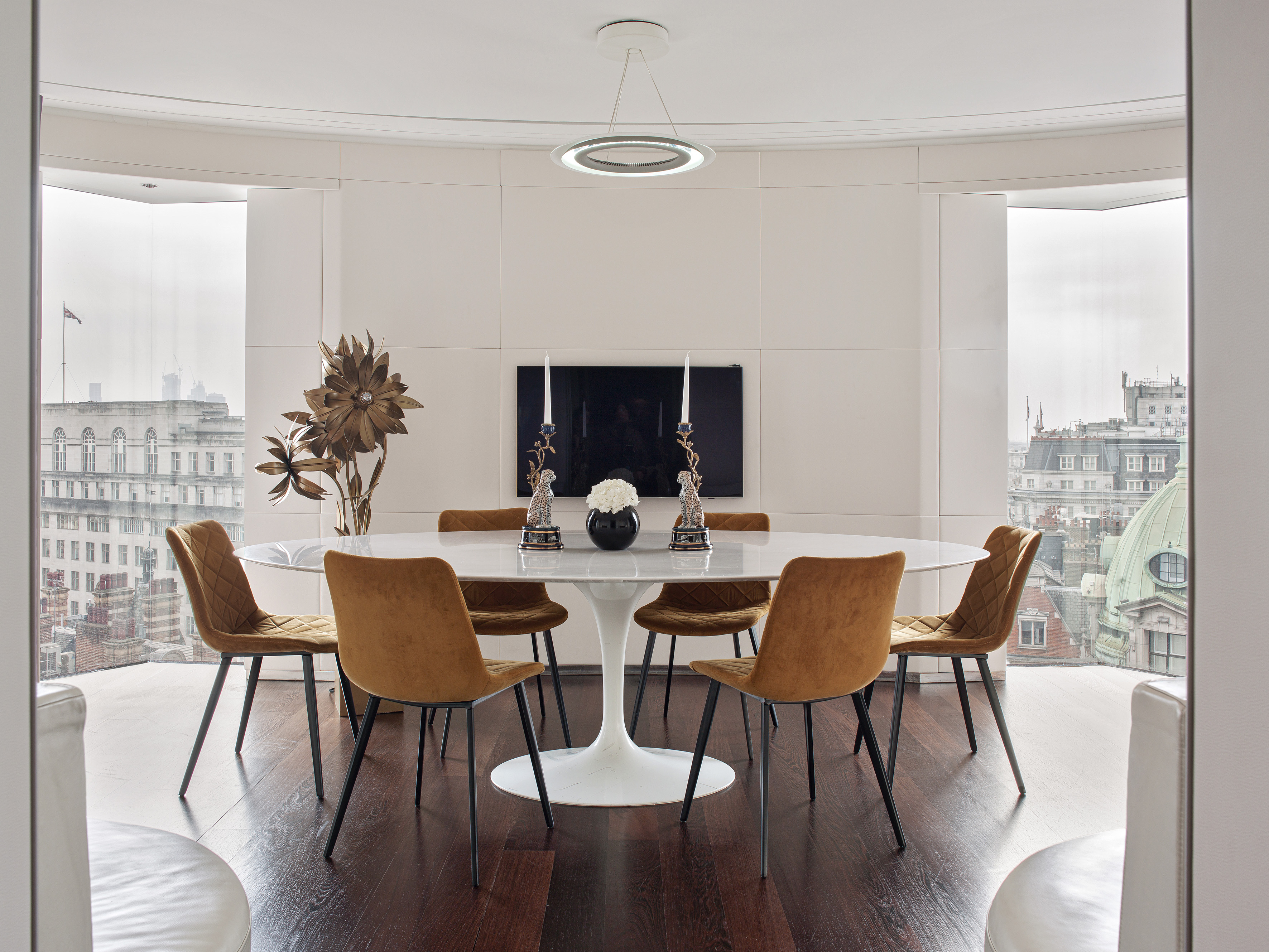 Modern dining room with oval marble table, velvet chairs, and city view.