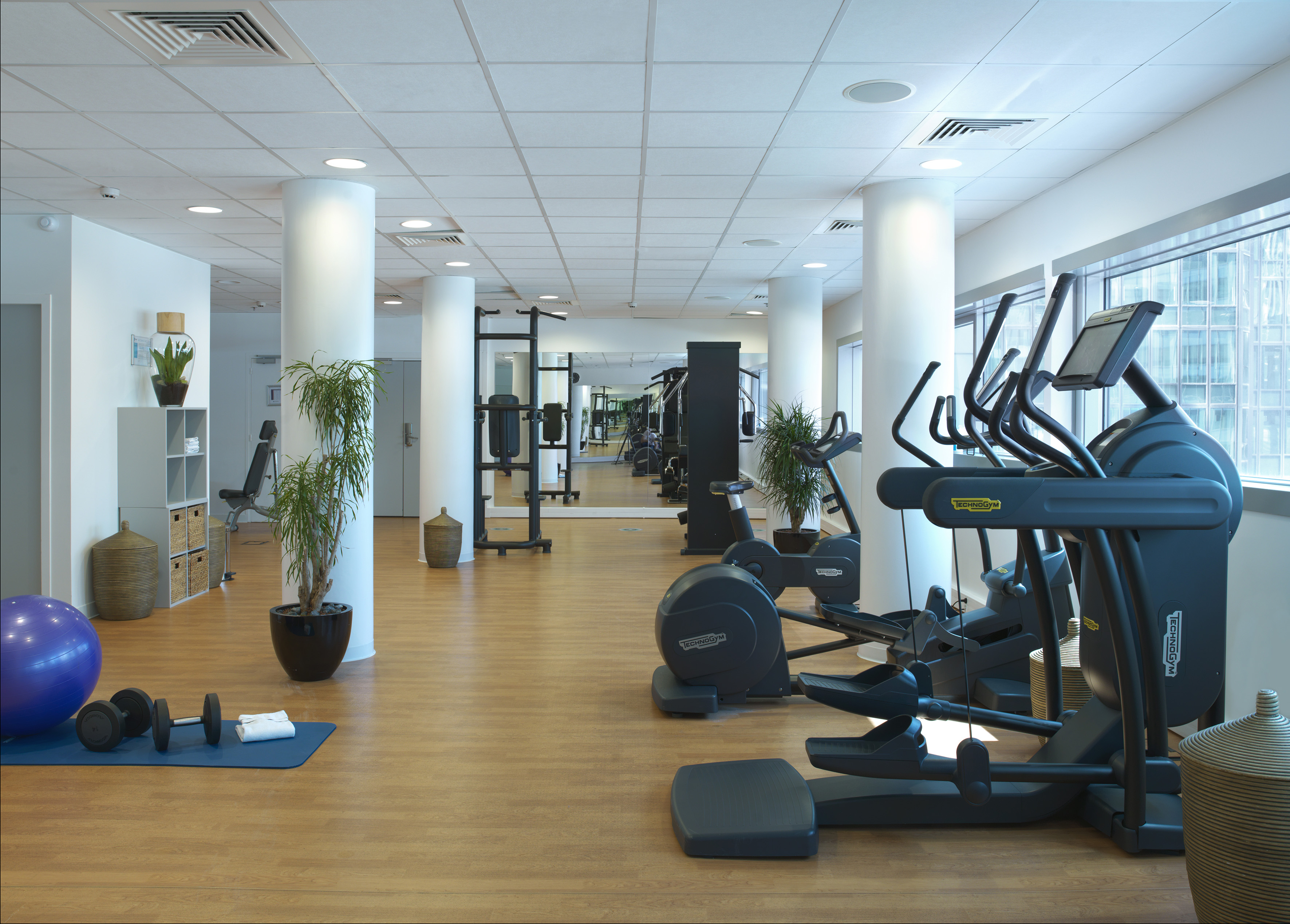 Modern hotel gym with Technogym ellipticals, weights, and large windows.
