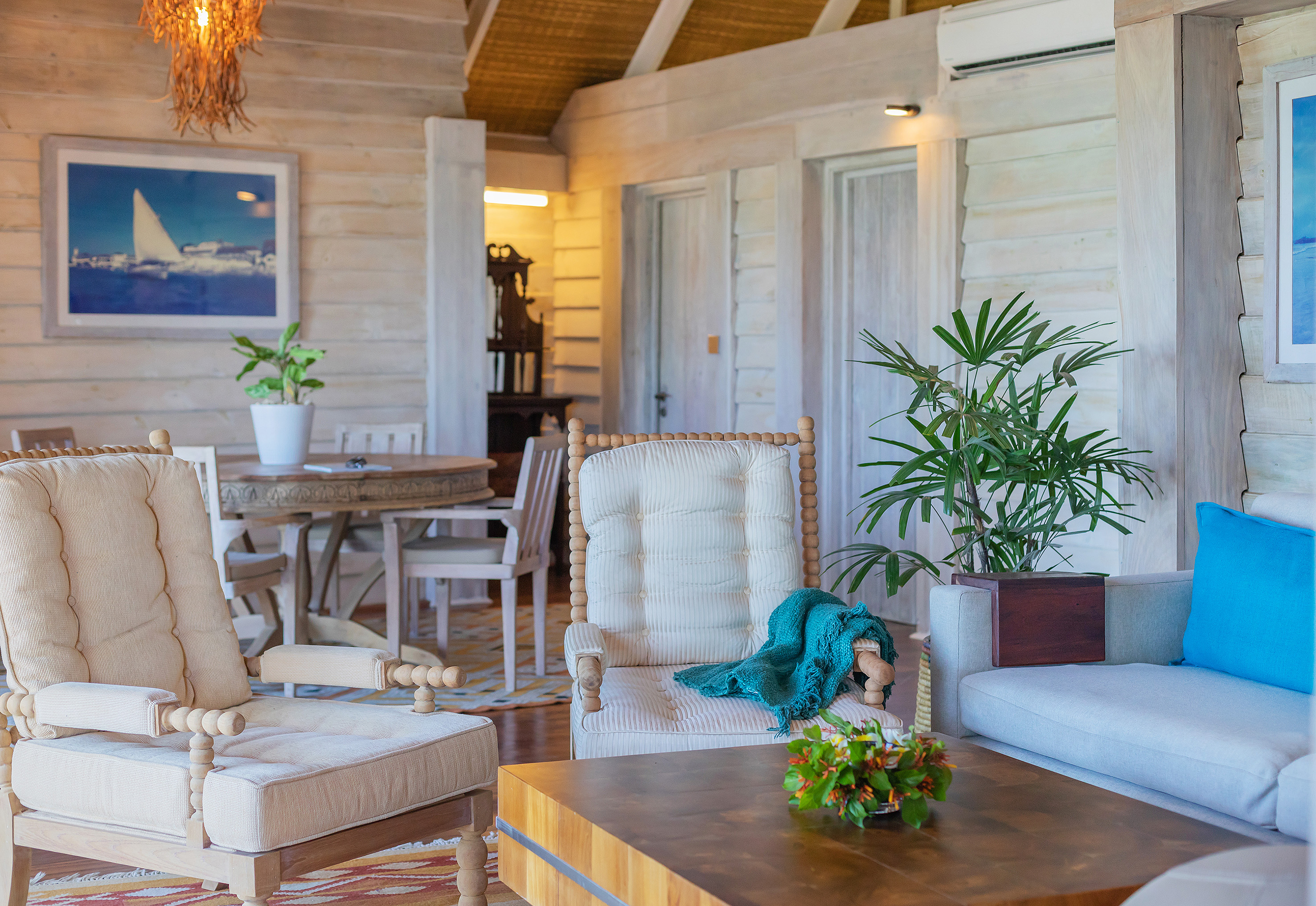 Tropical wooden living room with cushioned seating, dining area, and potted plants.
