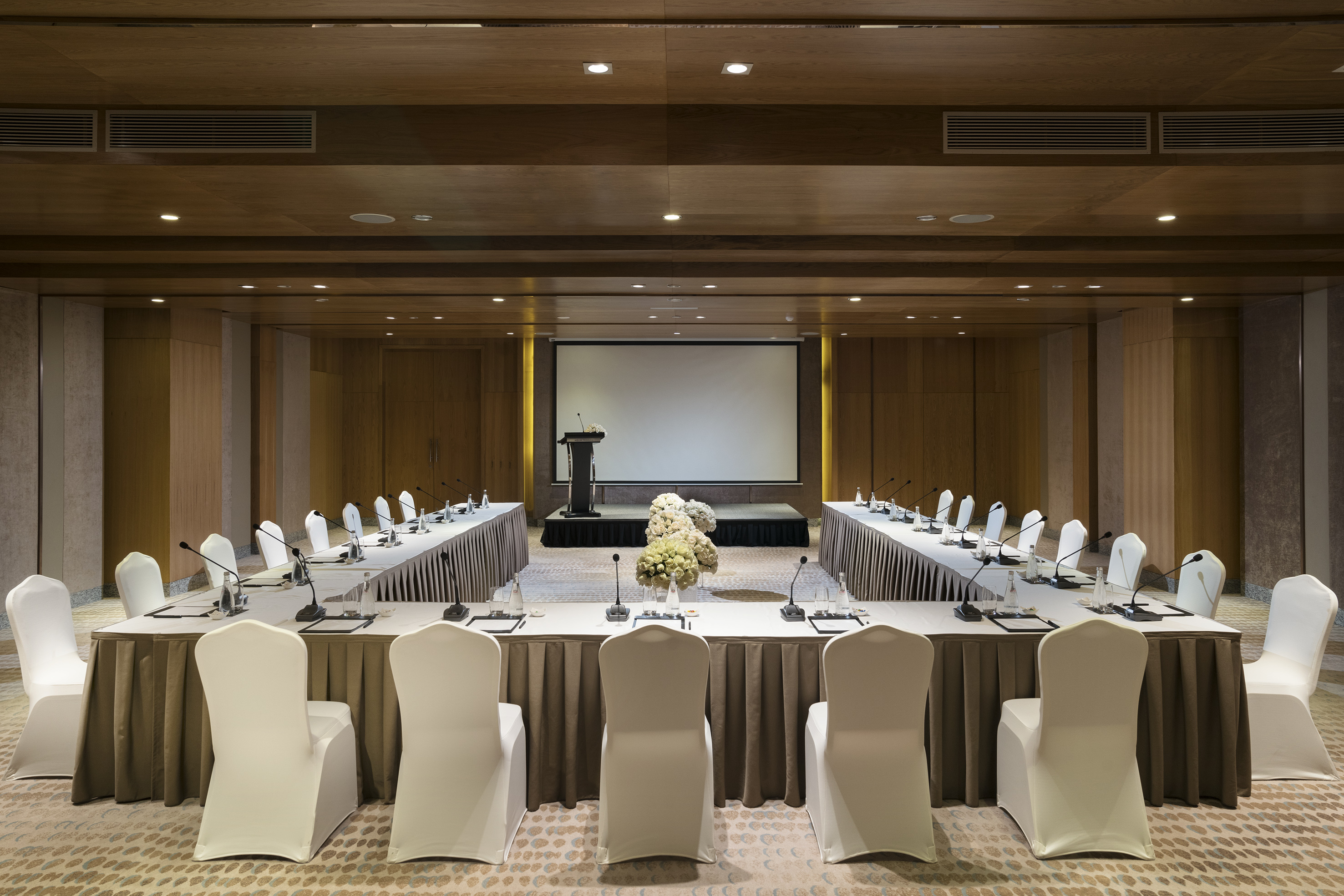 U-shaped meeting room setup with projector screen, lectern, and chairs.