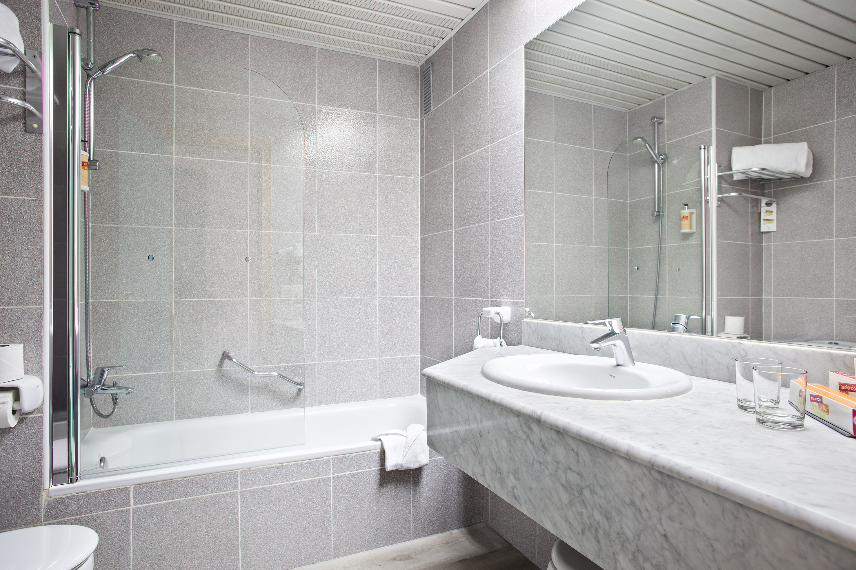 Hotel bathroom with gray tiles, white bathtub, shower, and marble sink.