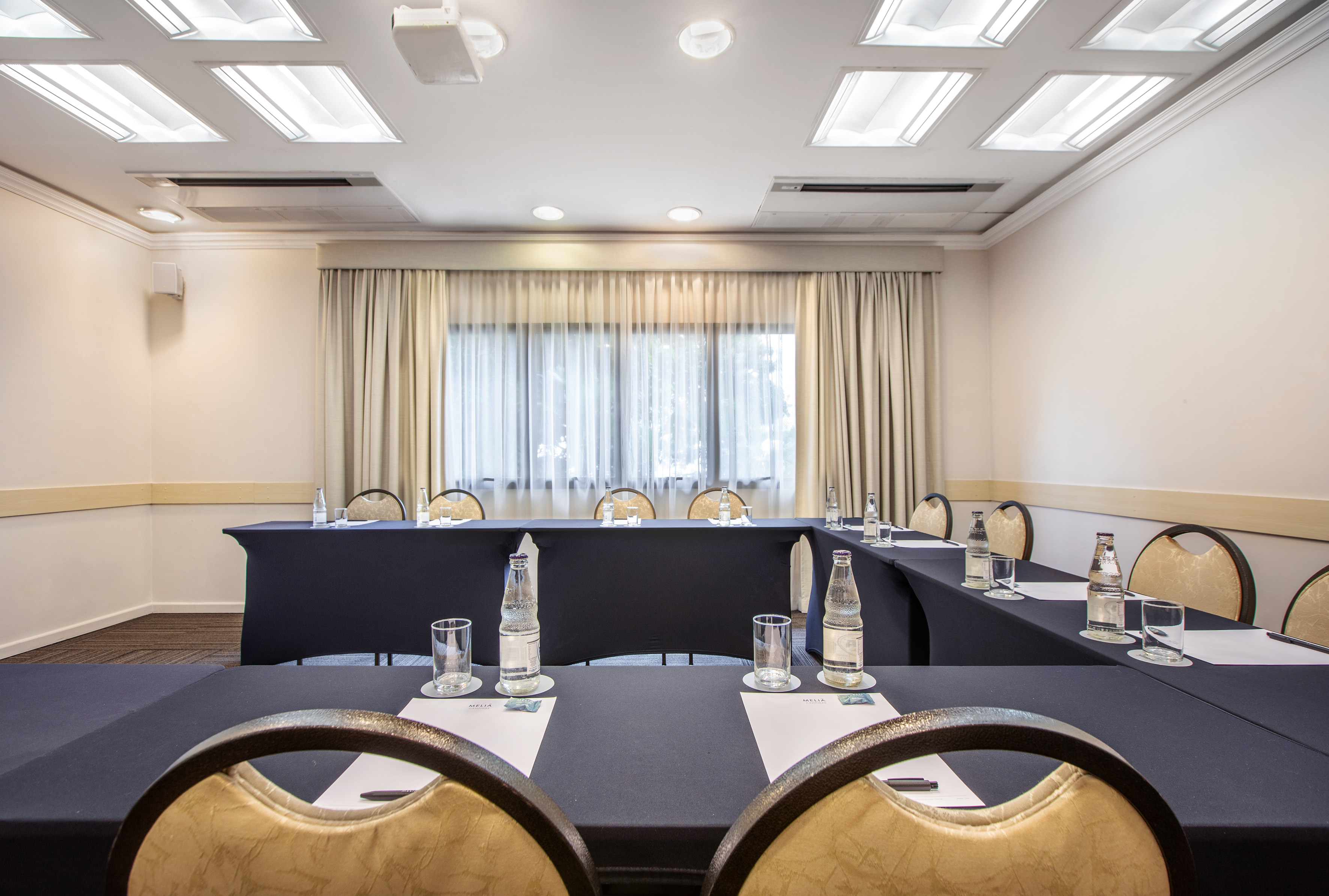 U-shaped meeting room setup with tables, chairs, water, and projector.