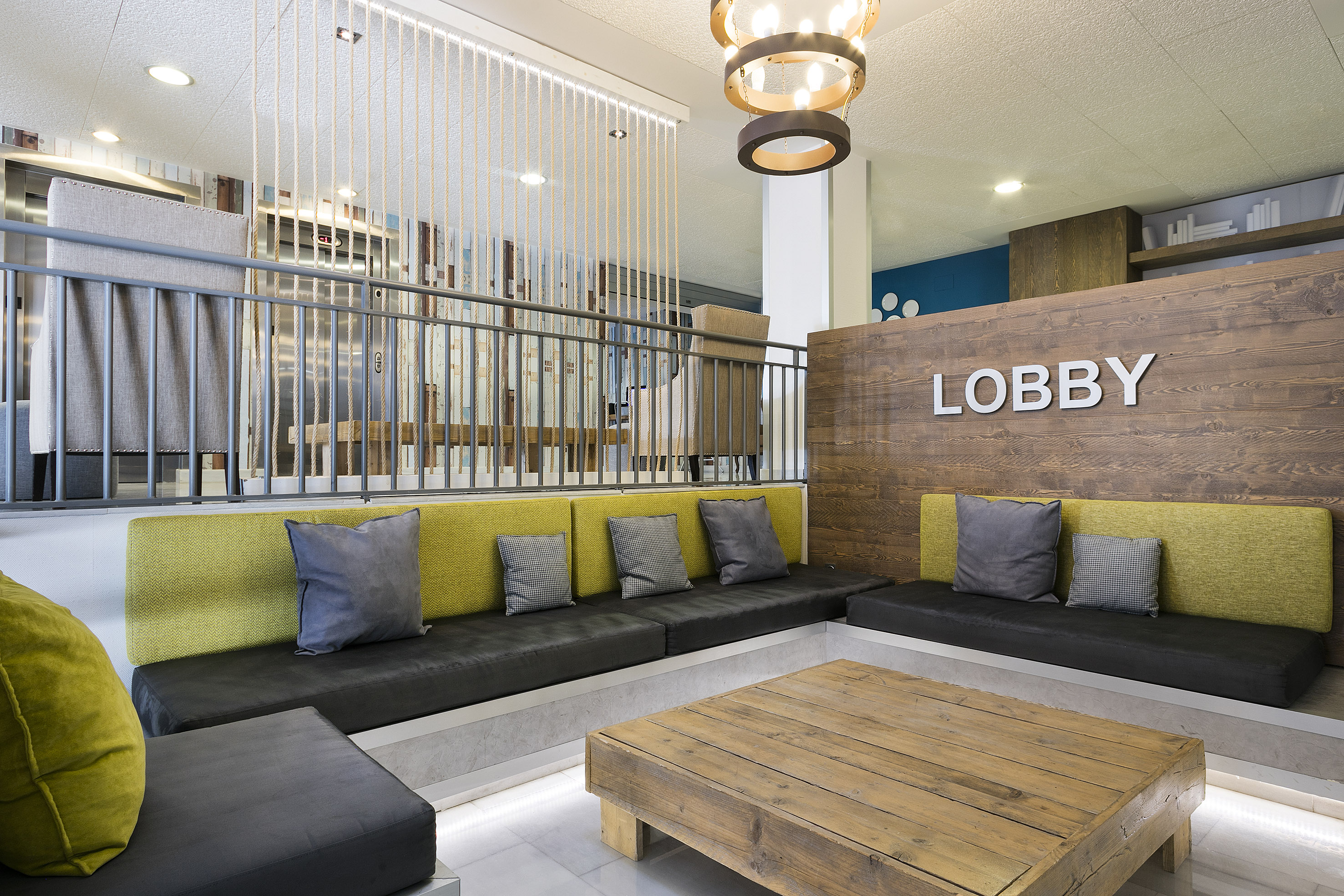 Modern hotel lobby with green seating, rustic wood table, and "LOBBY" sign.