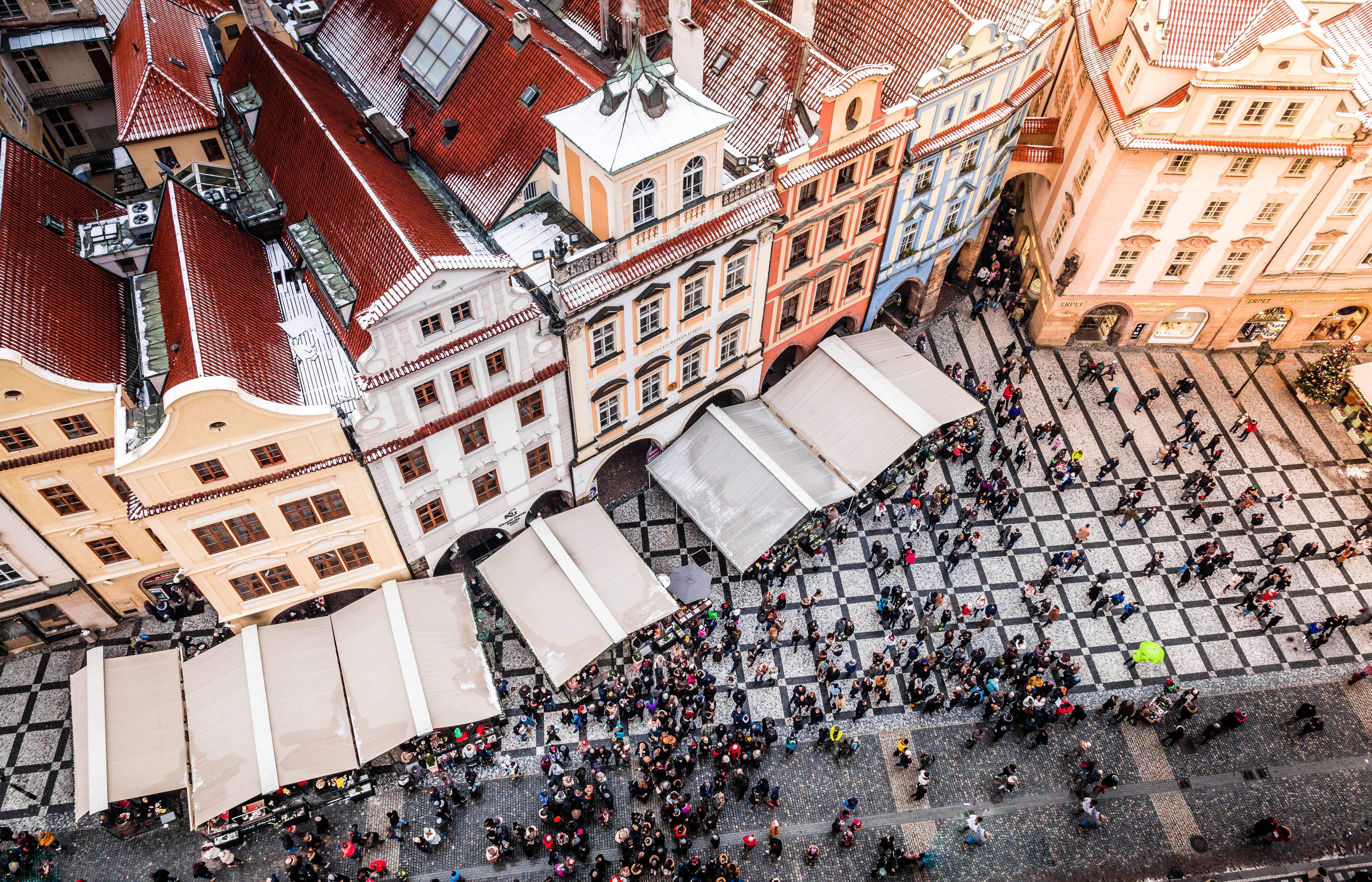 Aerial view Prague Old Town Square, snow on historic roofs, busy winter market crowd.