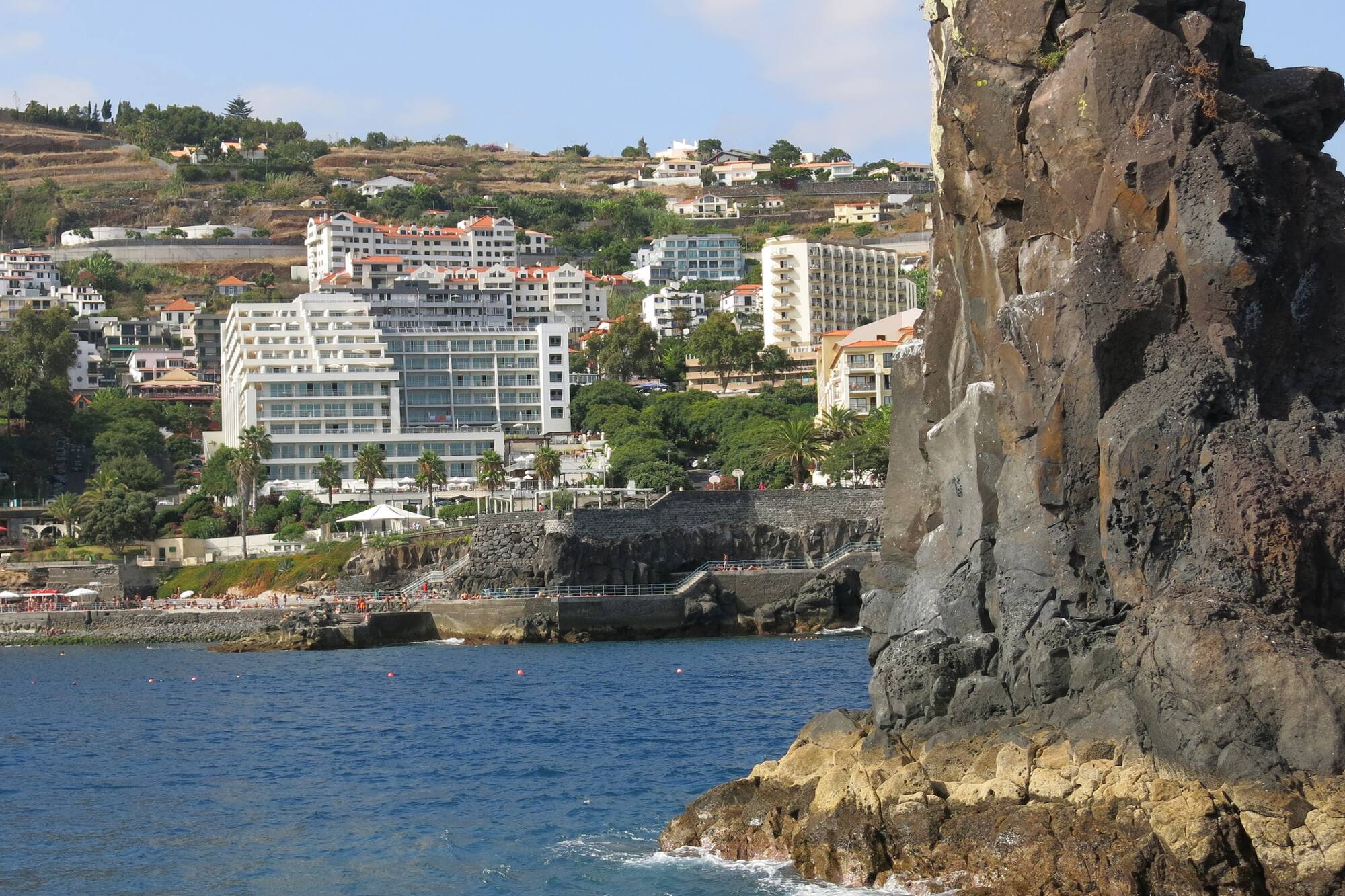 Large rock formation in ocean with Funchal Madeira hillside resort town.