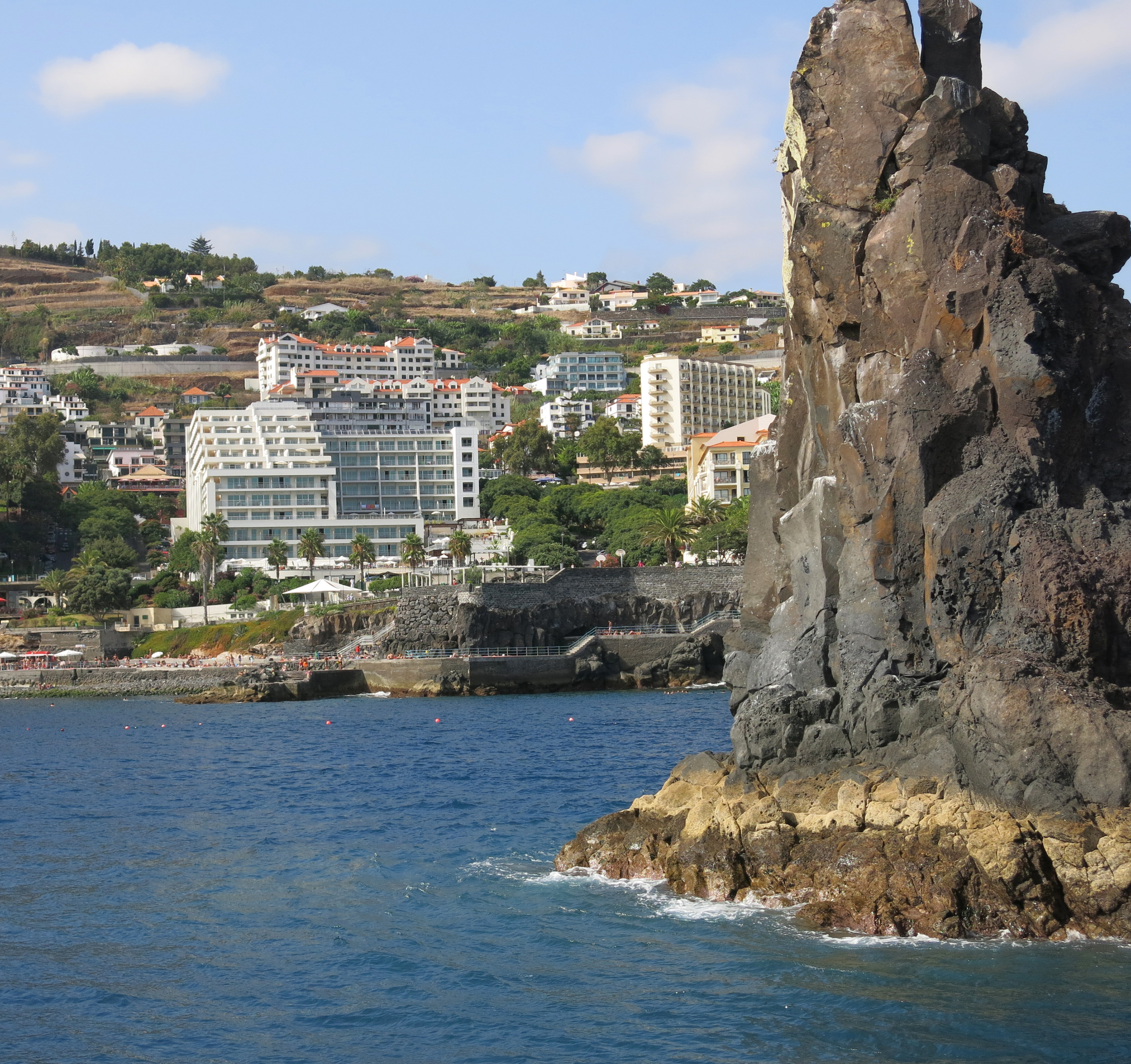 Large rock formation in ocean with Funchal Madeira hillside resort town.