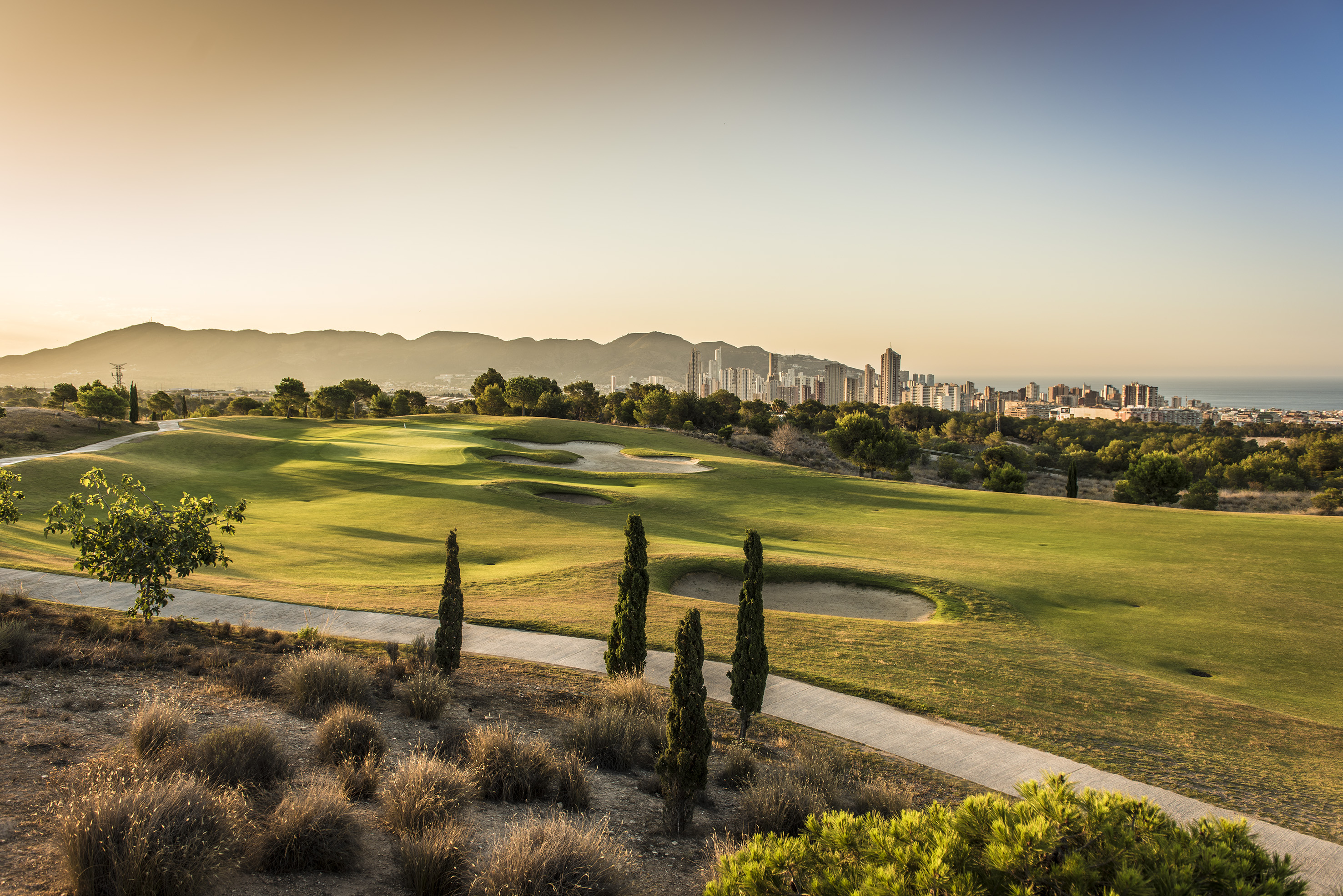 Benidorm golf course at sunset, city skyline, and Mediterranean Sea view.
