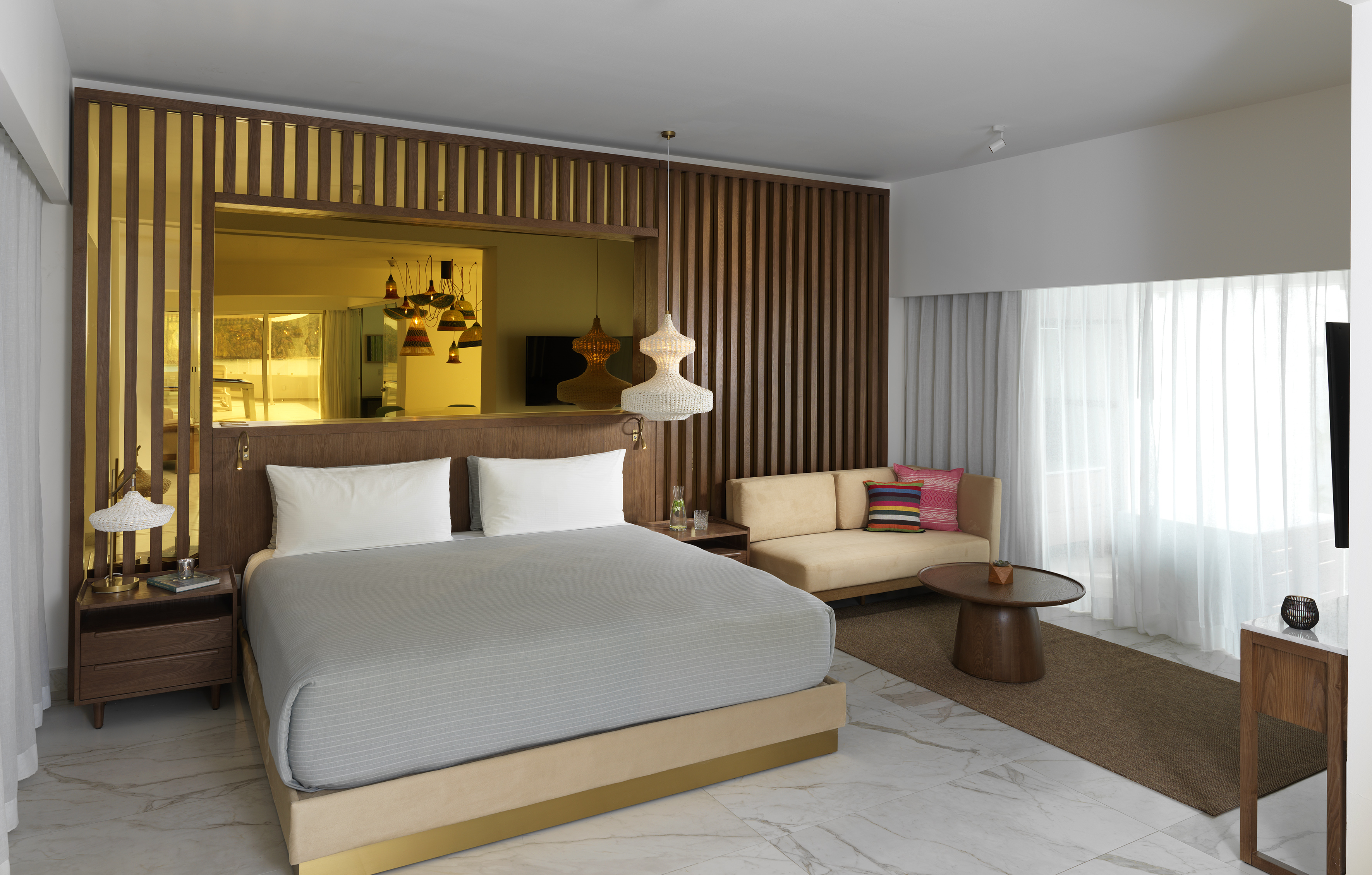 Modern hotel bedroom with king bed, wood accents, sofa, and marble floor.