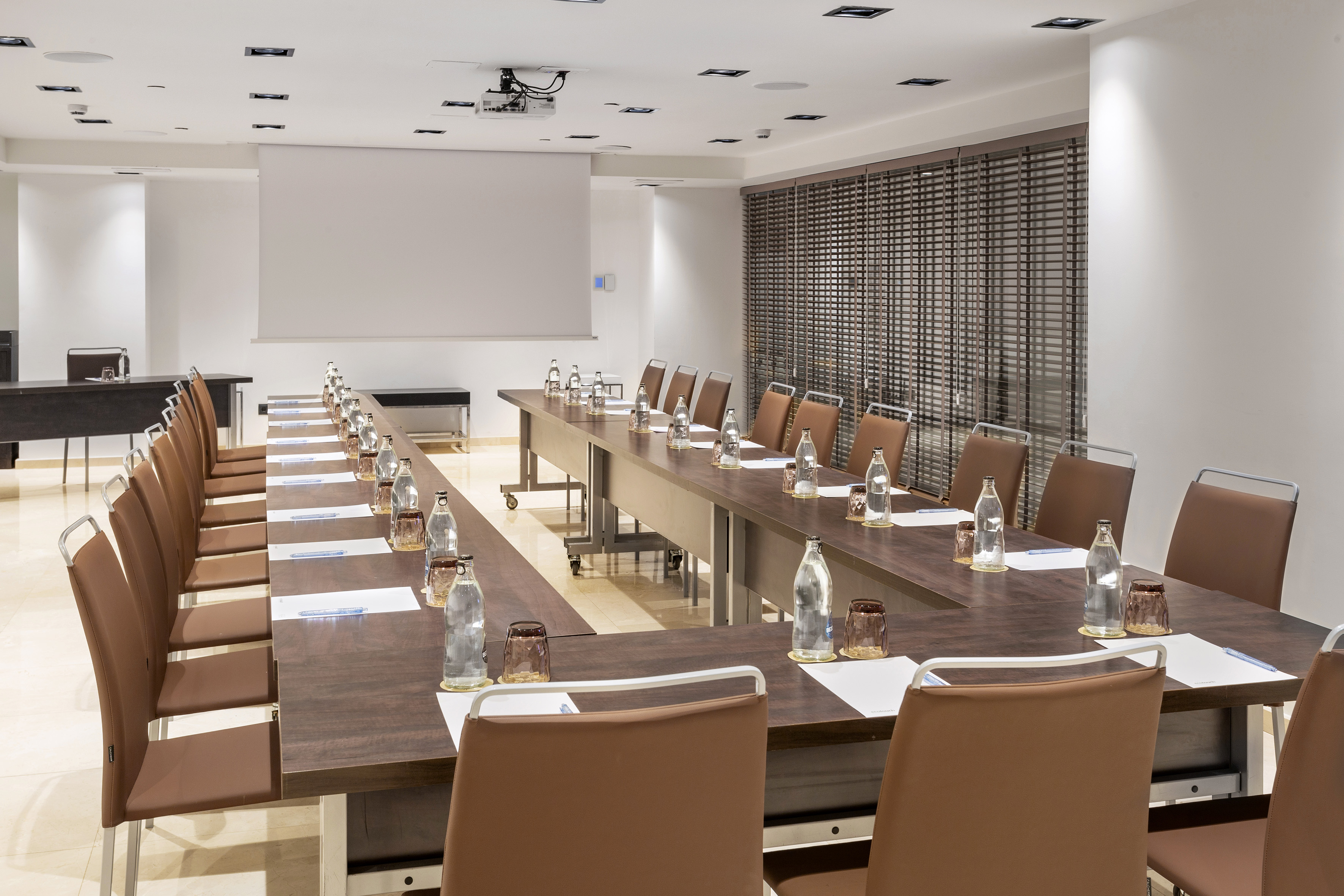 Modern U-shape conference room with projector, screen, and water bottles for meetings.