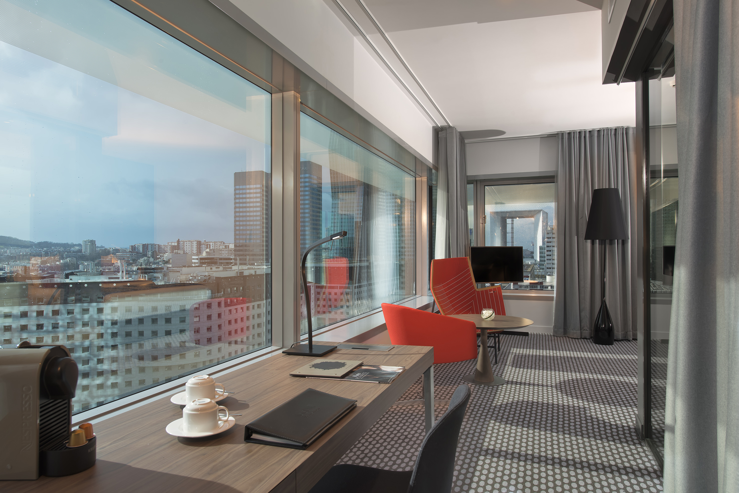 Contemporary hotel room with panoramic city view, desk, and Nespresso machine.