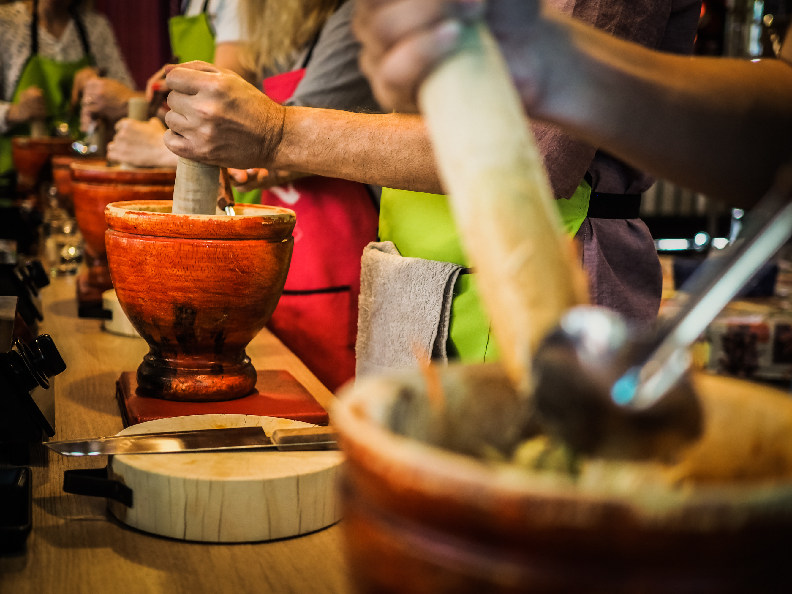 Hands using wooden pestles in orange mortars during a cooking class.
