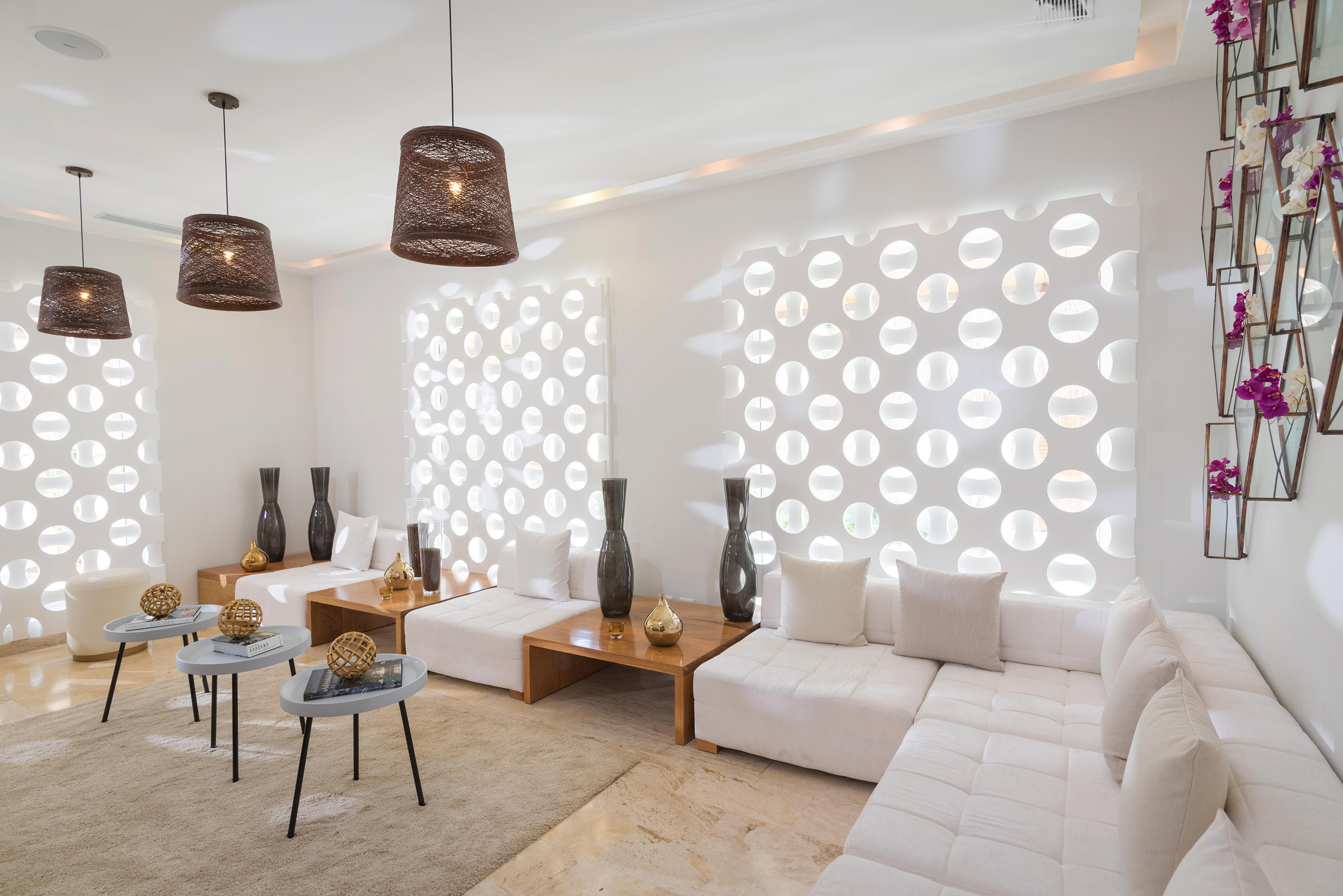 Sleek white lounge with modular sofas, rattan pendants, and geometric wall.