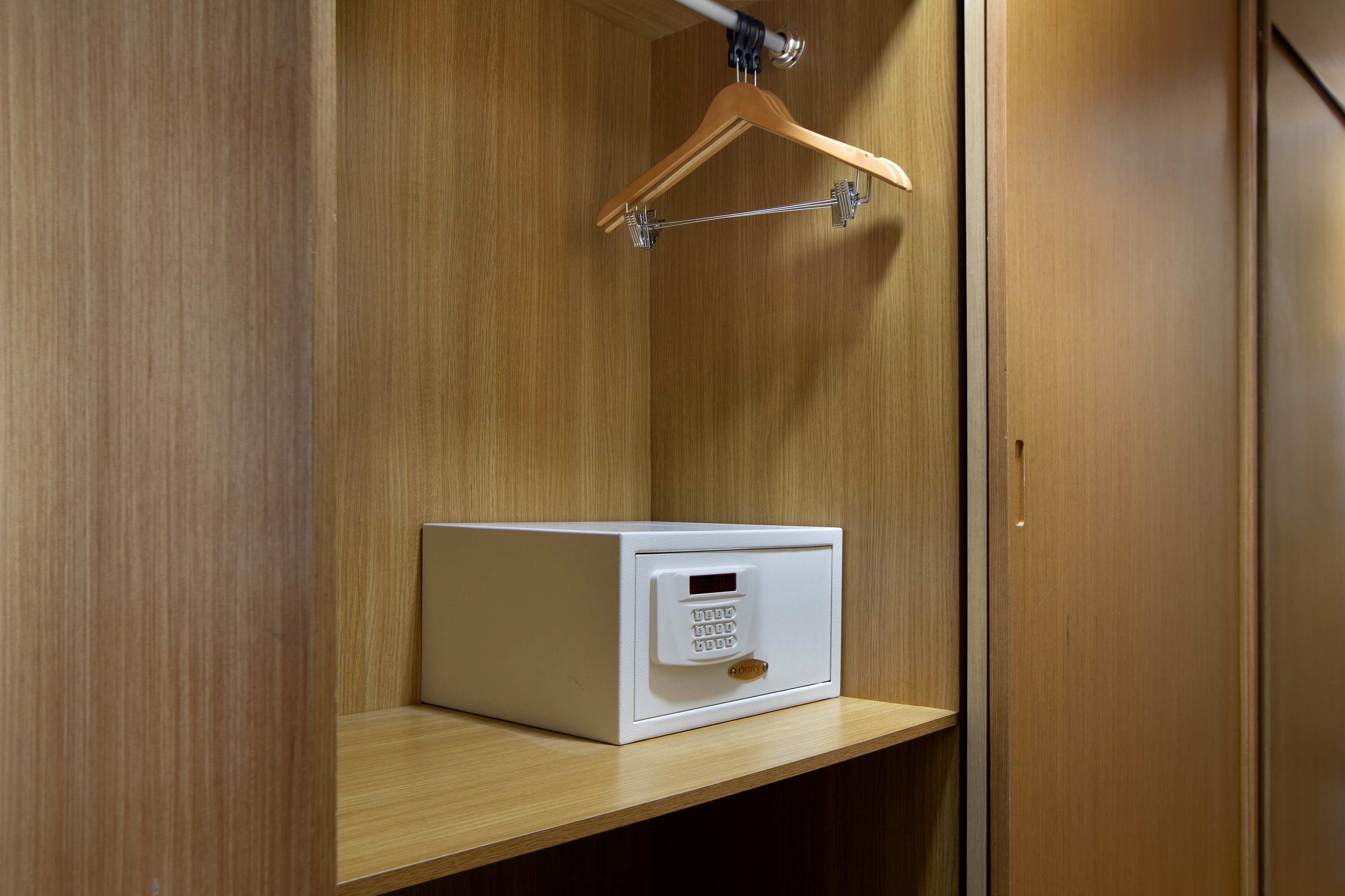 White digital hotel safe inside a wooden wardrobe with a hanger.
