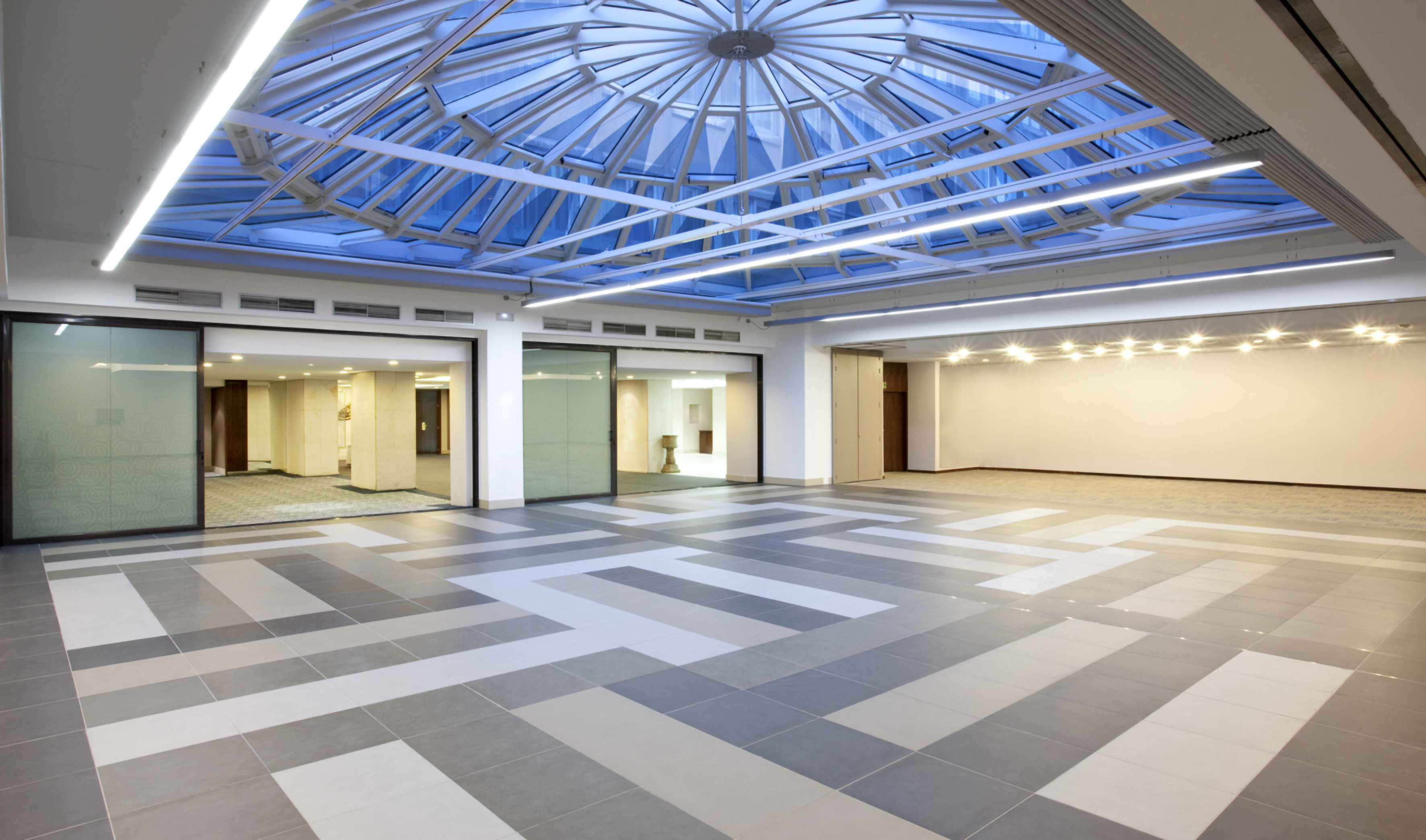 Spacious modern hall with patterned floor, glass skylight, and bright lights.