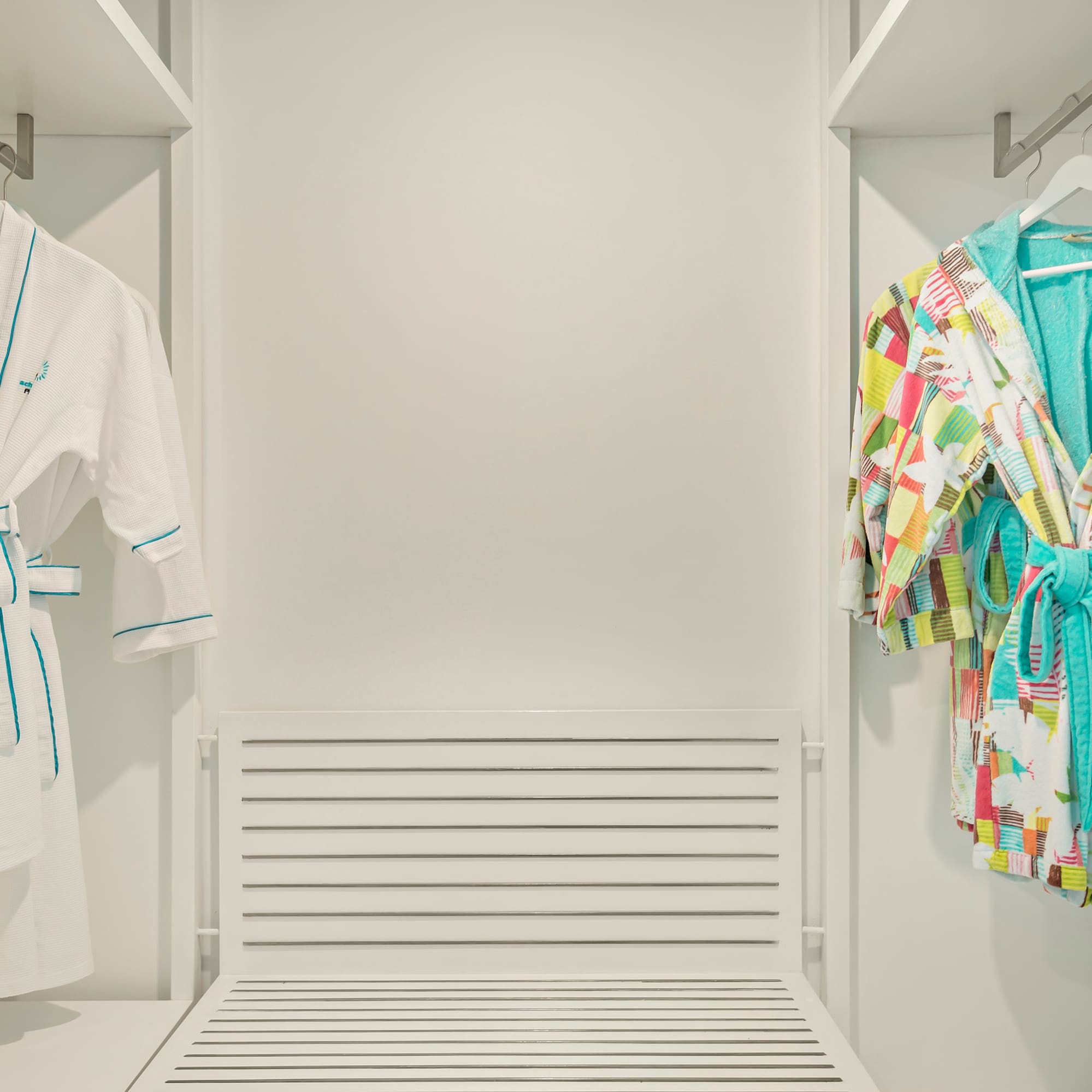a closet with white walls and white shelves with colorful robes on swingers