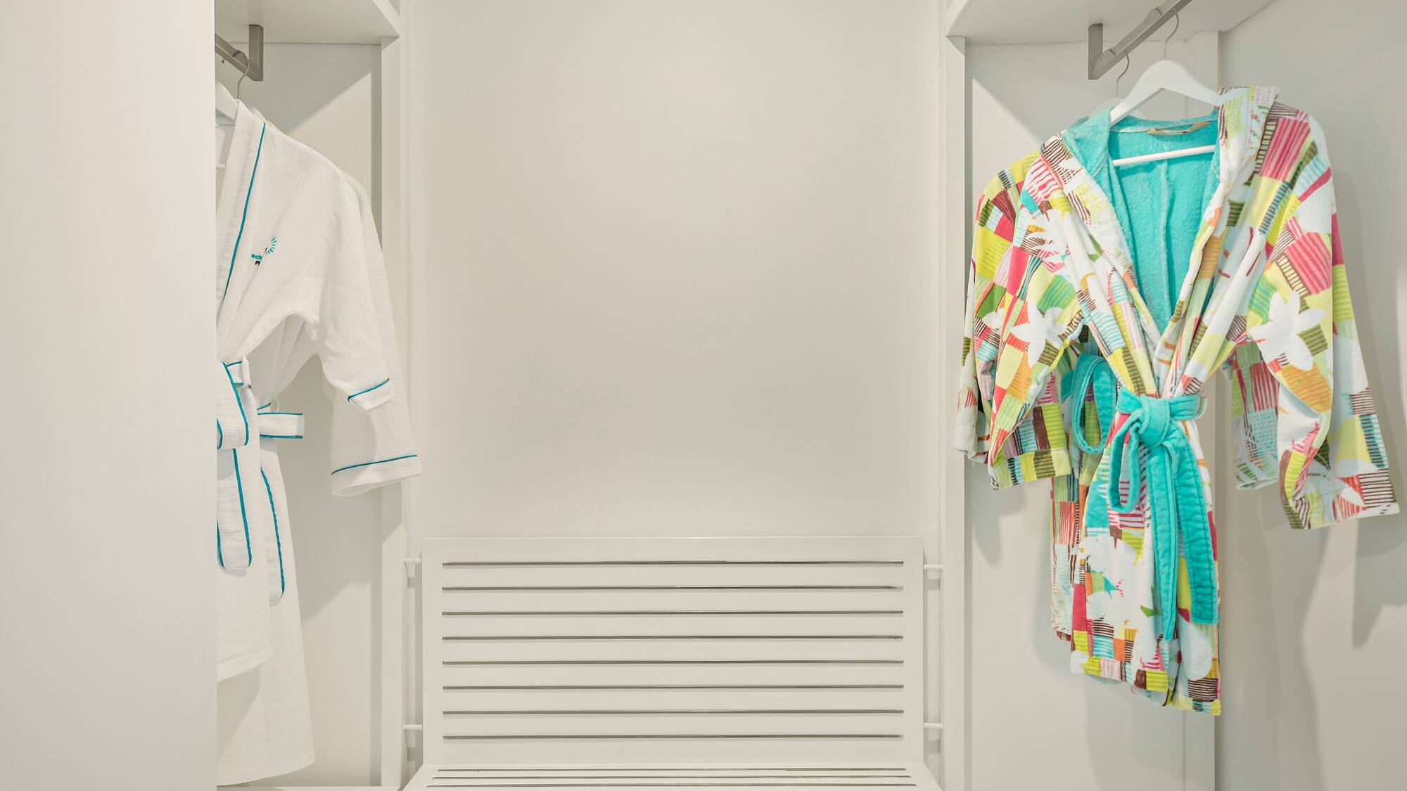 a closet with white walls and white shelves with colorful robes on swingers