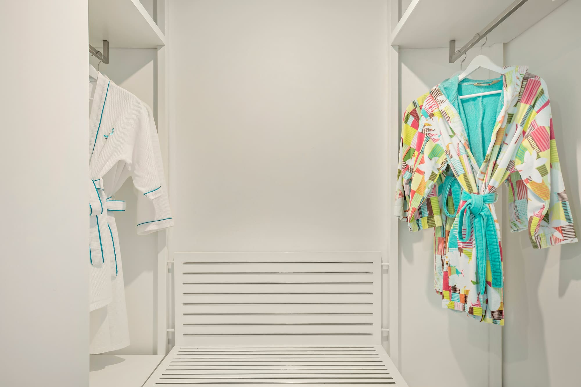 a closet with white walls and white shelves with colorful robes on swingers