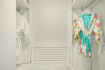 a closet with white walls and white shelves with colorful robes on swingers