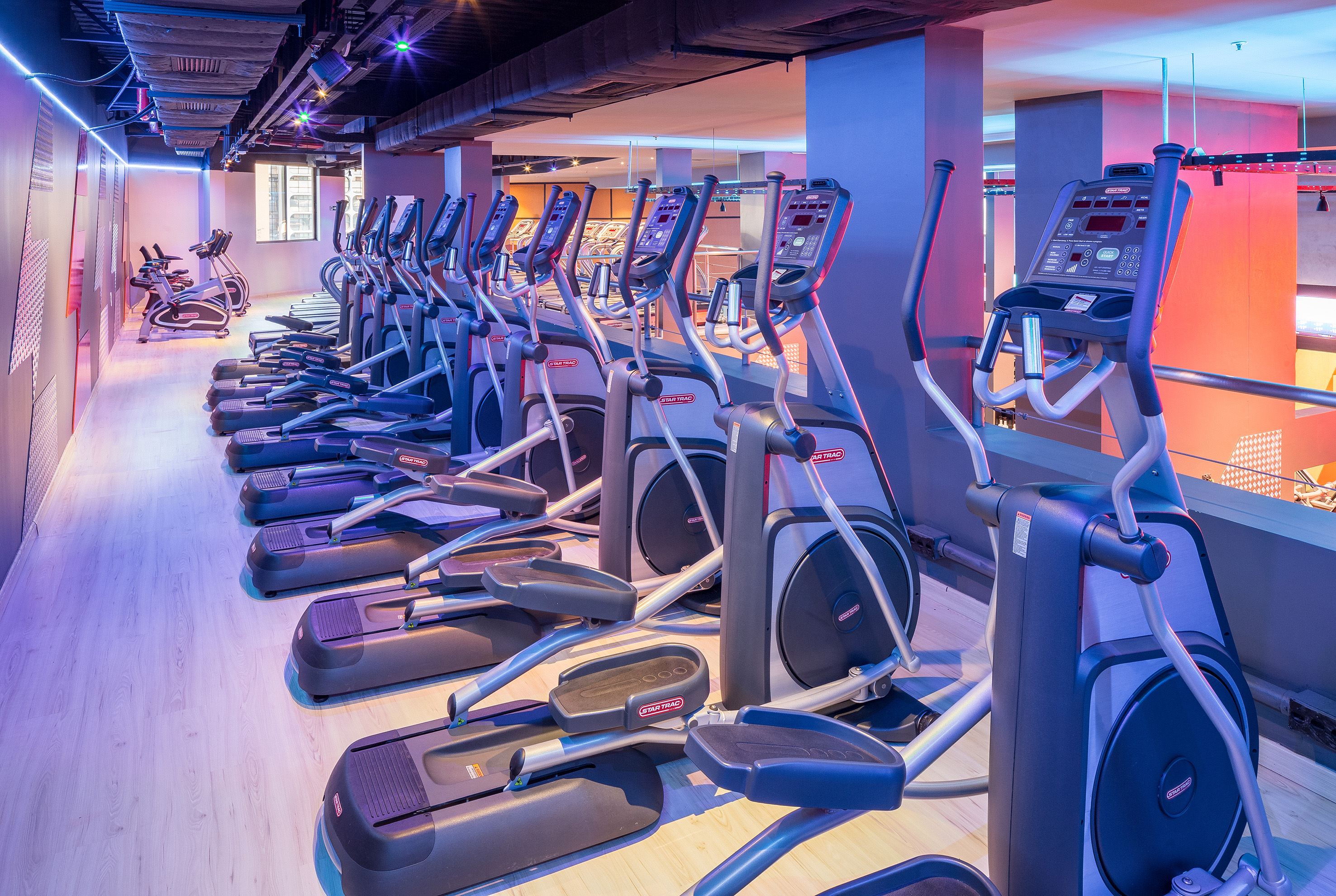 Row of Star Trac elliptical machines in a modern gym with blue and red lighting.