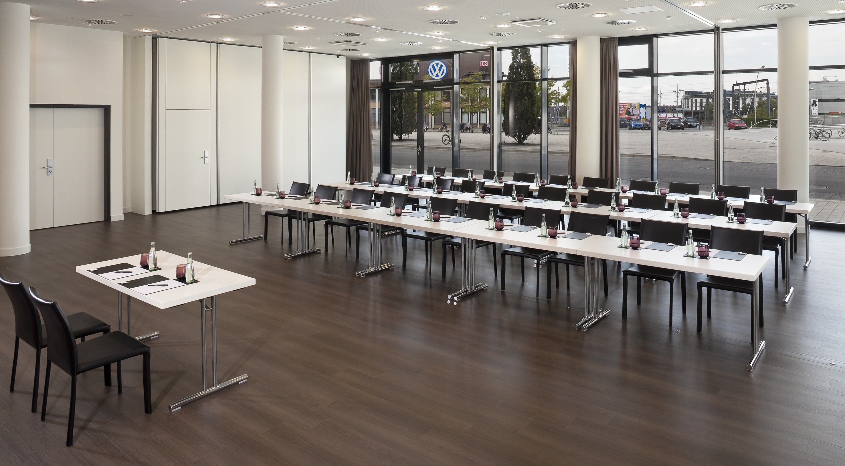 Modern corporate conference room with tables, chairs, and large windows.