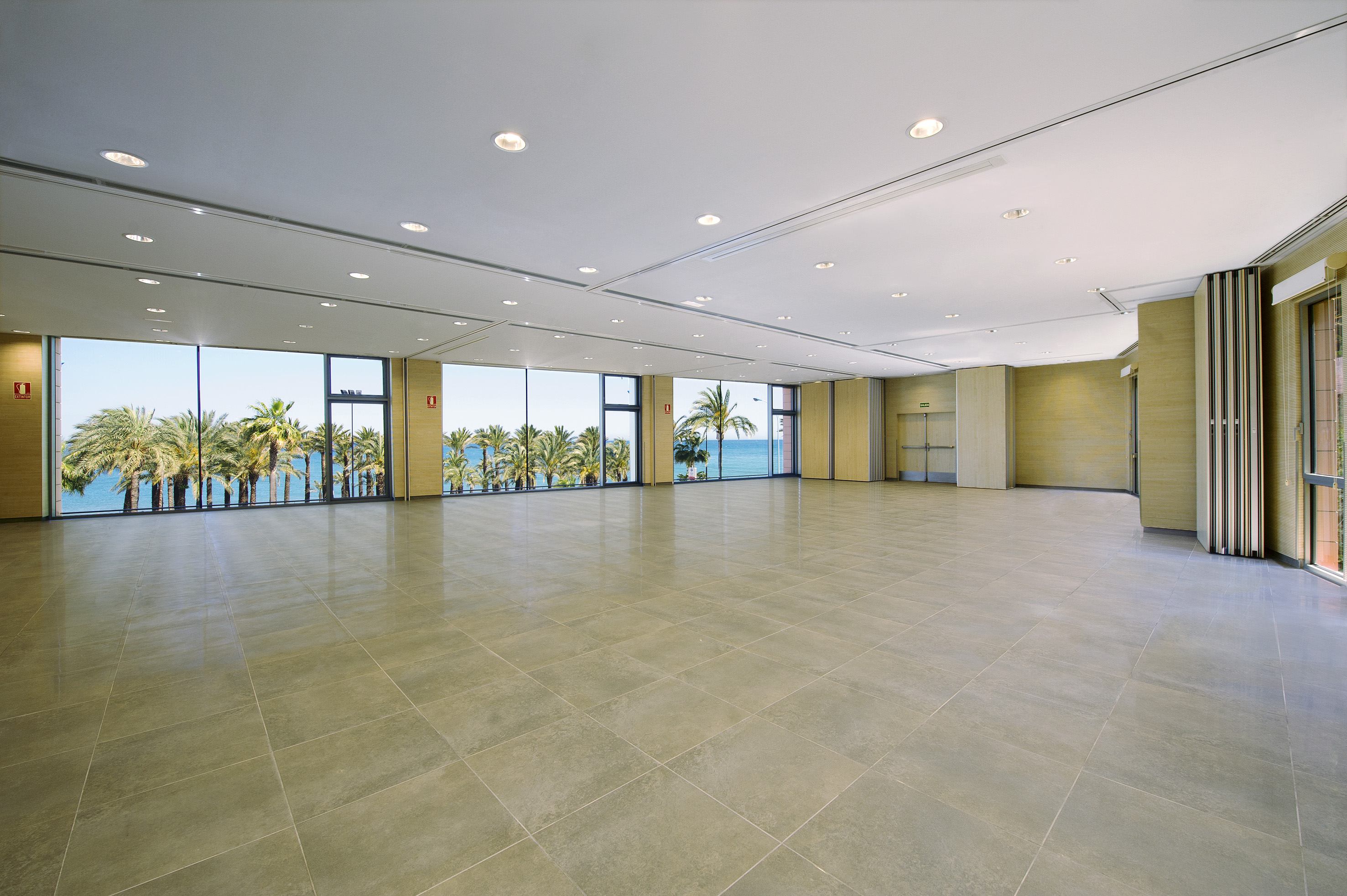 Spacious empty conference hall with tropical sea view and large windows.