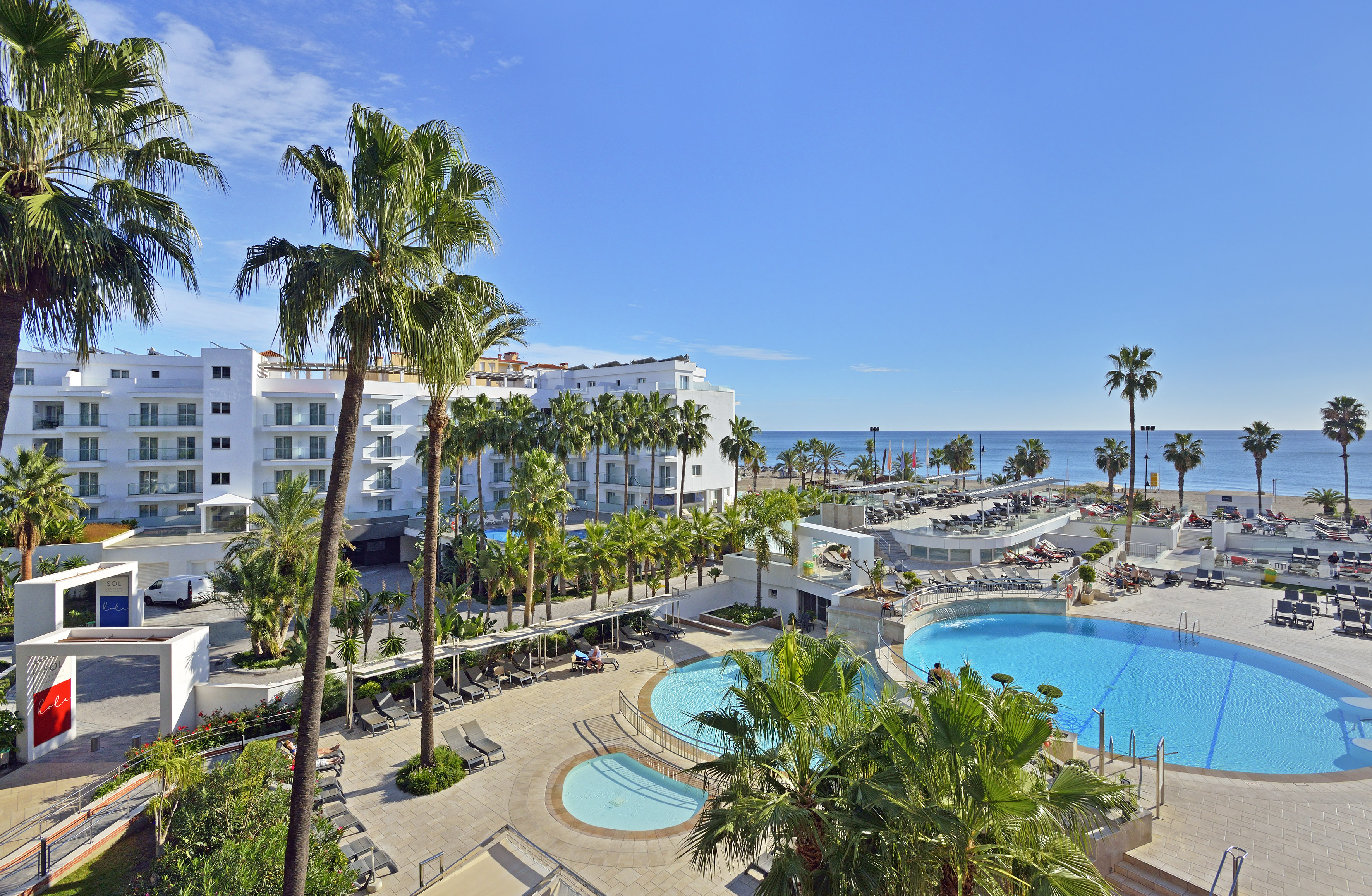 Sunny beachfront resort hotel with pools, palm trees, and ocean.