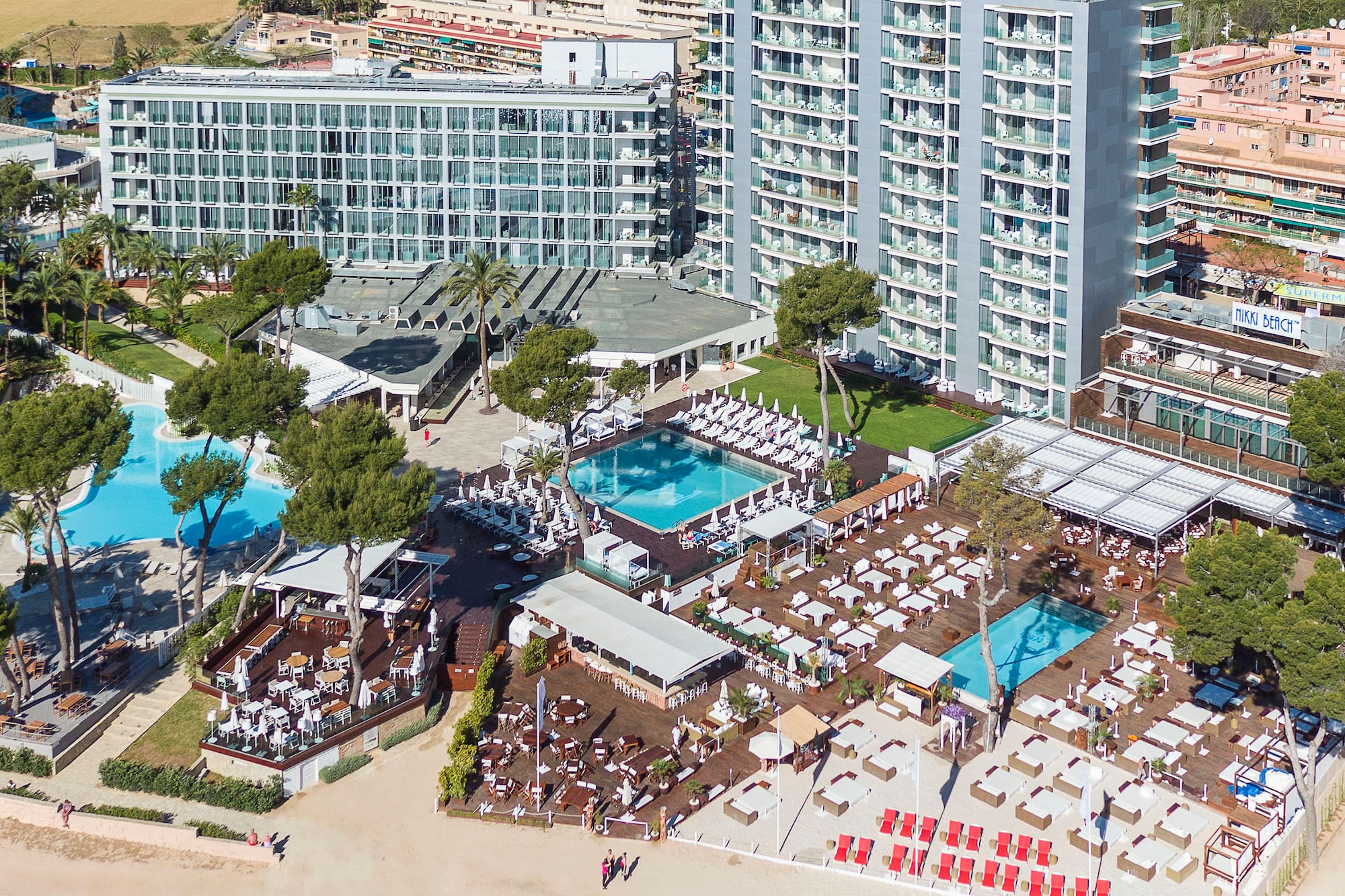 Aerial of beachfront hotel resort with pools, outdoor lounges, and sandy beach.