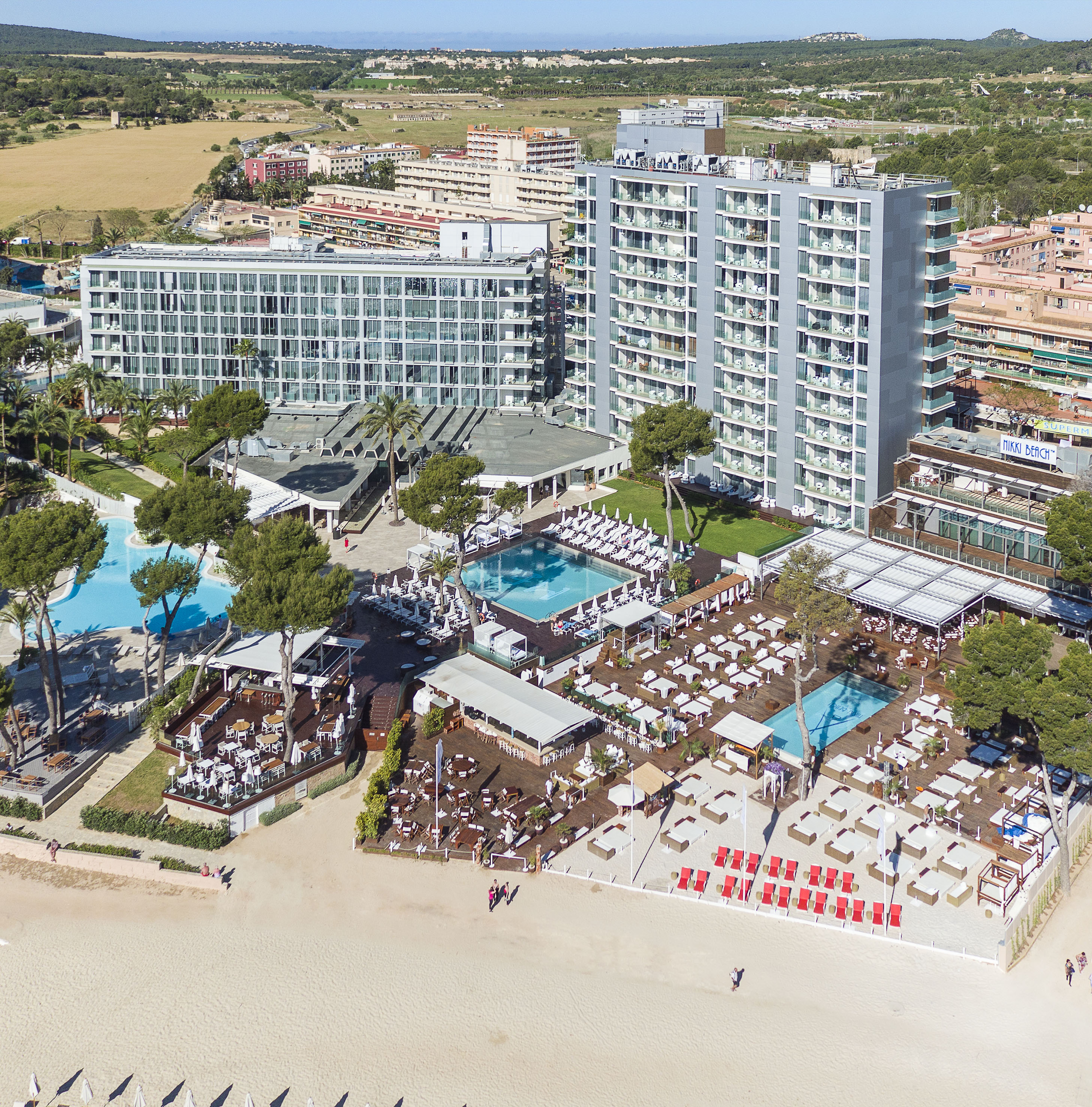Aerial of beachfront hotel resort with pools, outdoor lounges, and sandy beach.