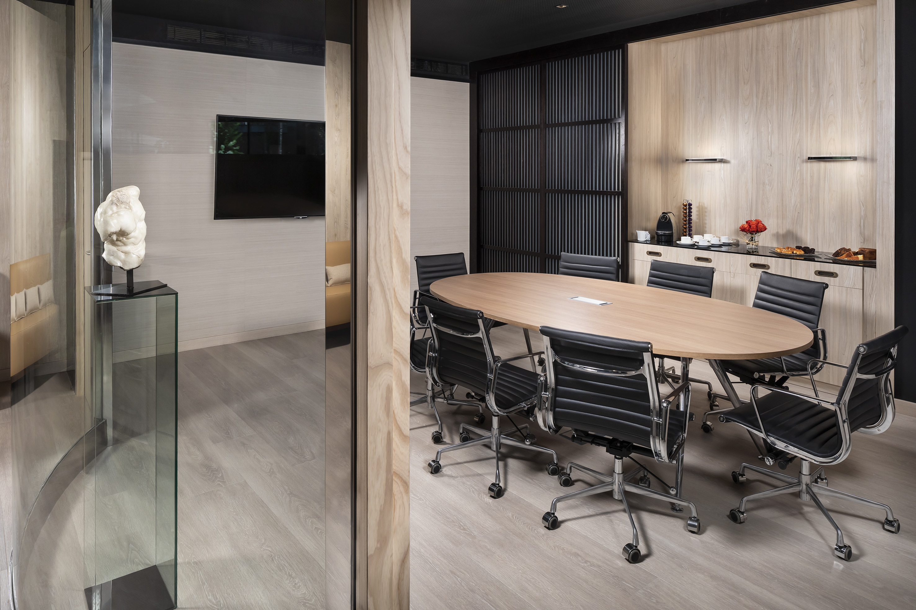 Modern meeting room with oval wooden table, black chairs, and refreshment area.