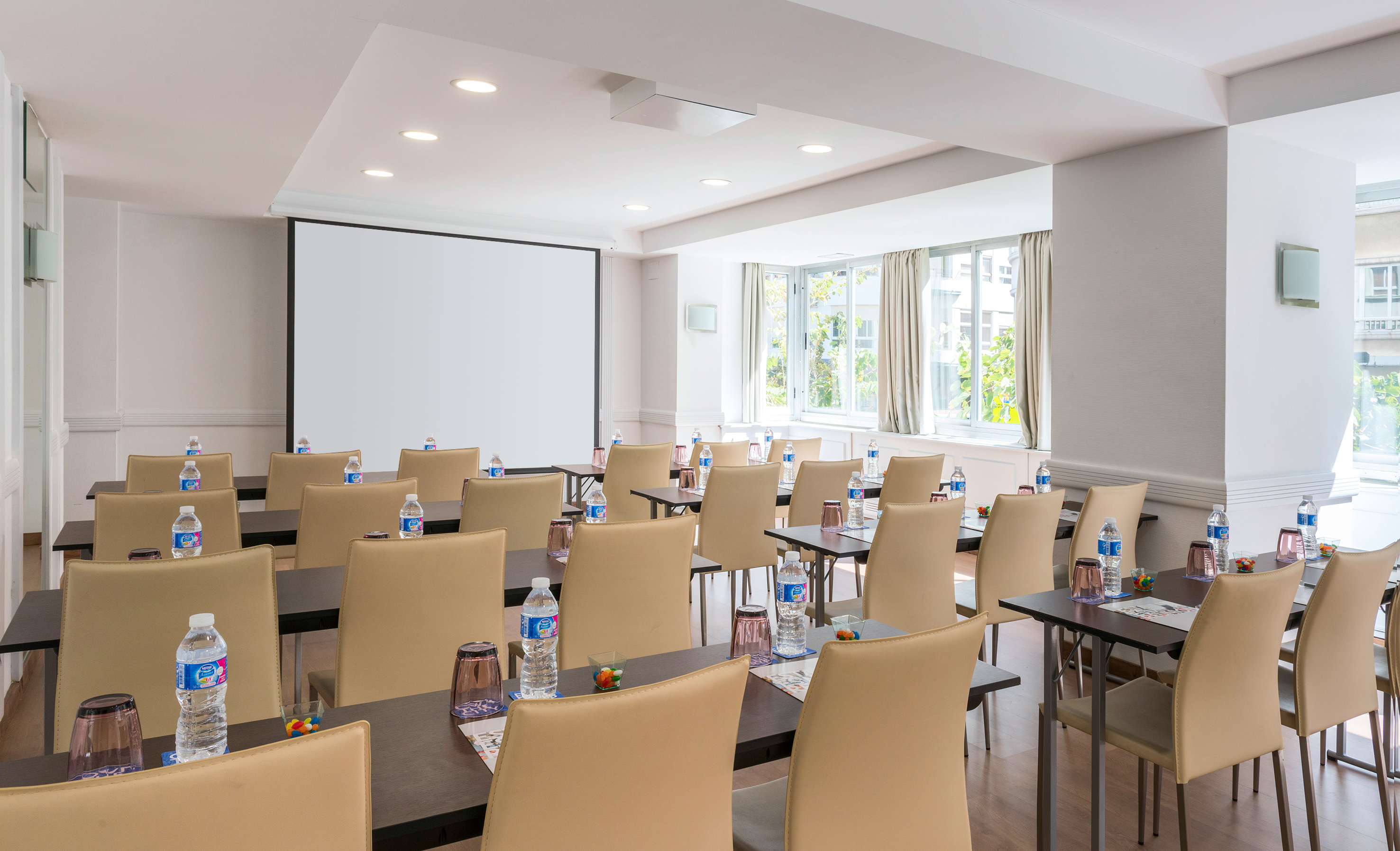 Bright conference room with screen, tables, beige chairs, and water setup. - Postiguet - Hotel Alicante Gran Sol Affiliated by Meliá, 阿利坎特