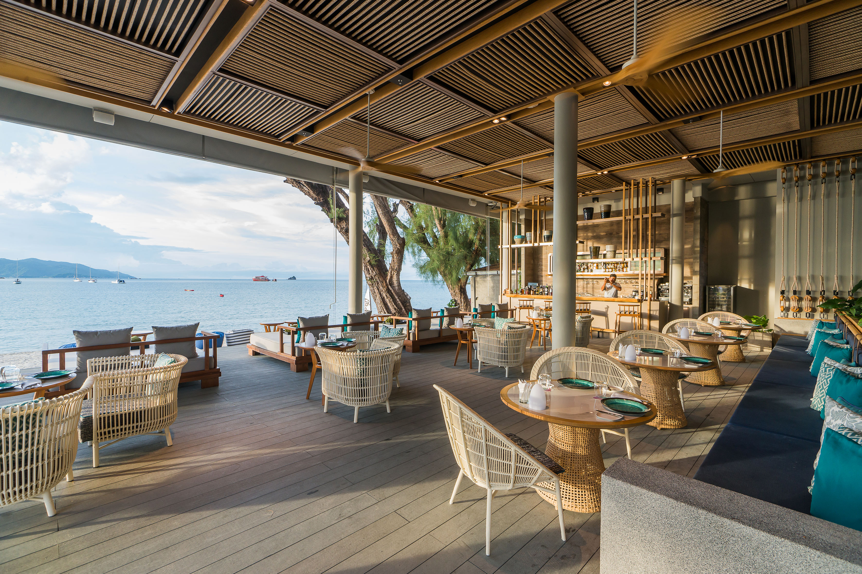 Beachfront dining area with rattan furniture, a bar, and ocean view.