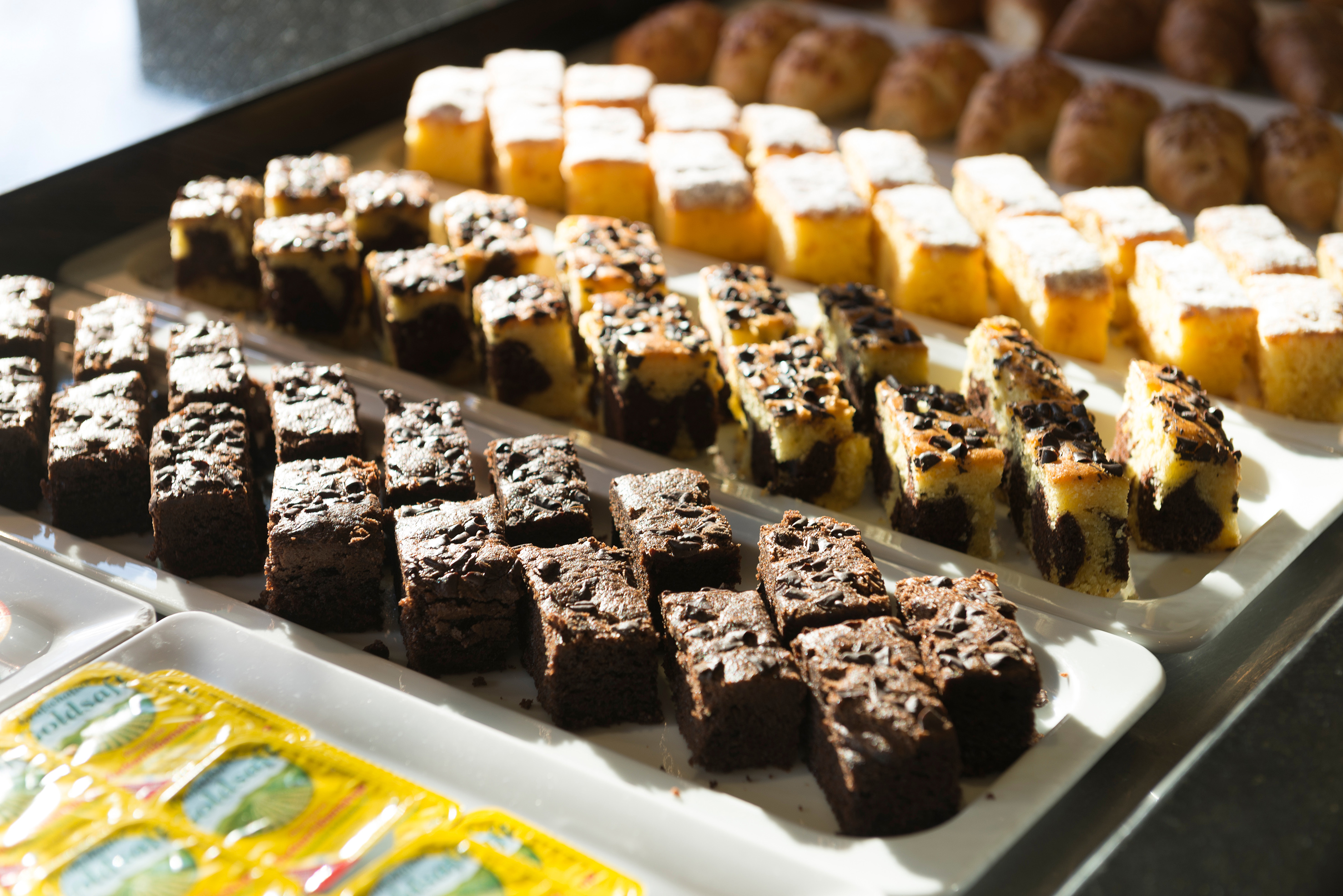 Rows of brownies, marble cakes, and yellow cakes on a dessert buffet.
