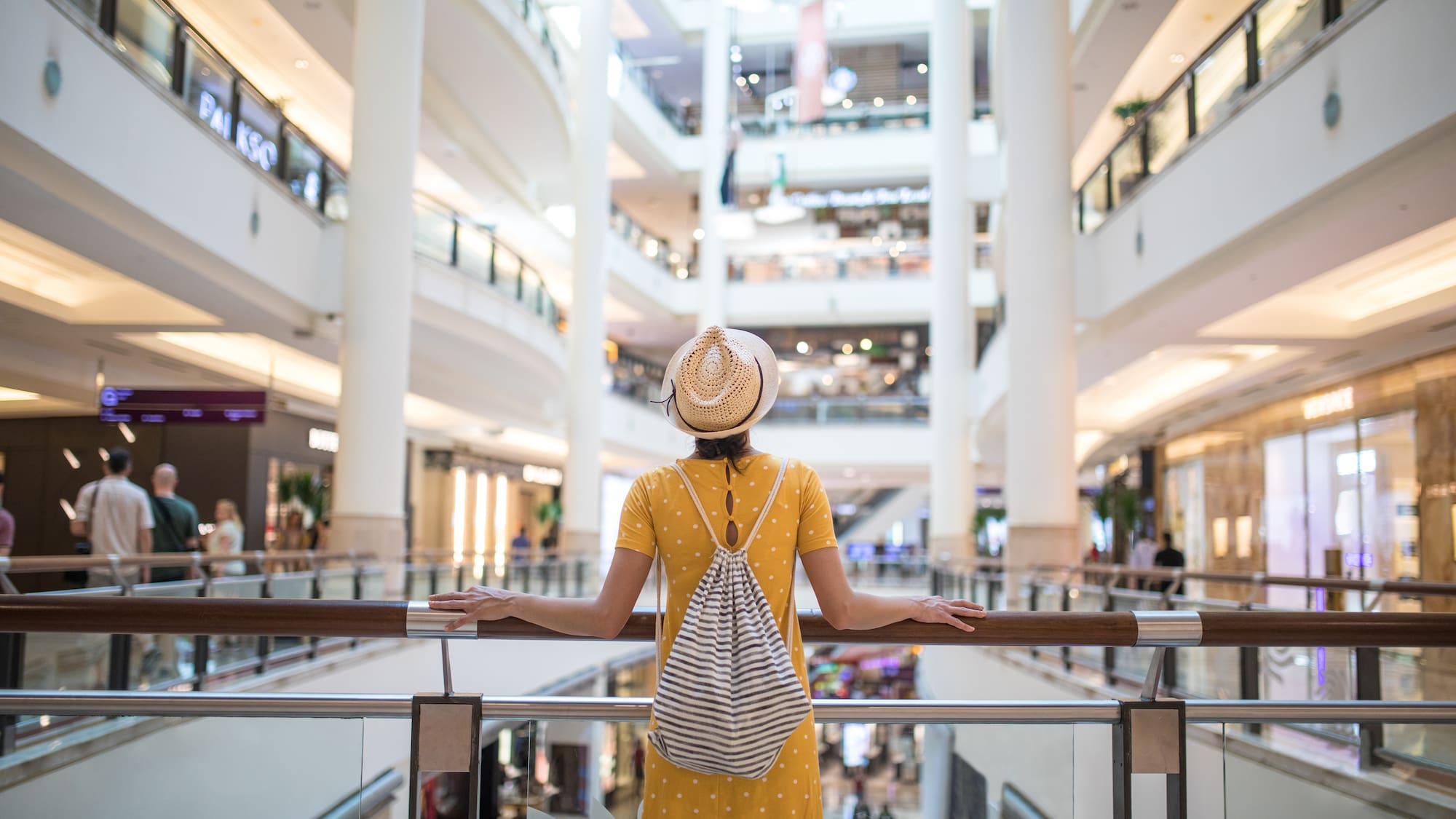 a woman in a yellow dress and hat standing by a railing in a large building