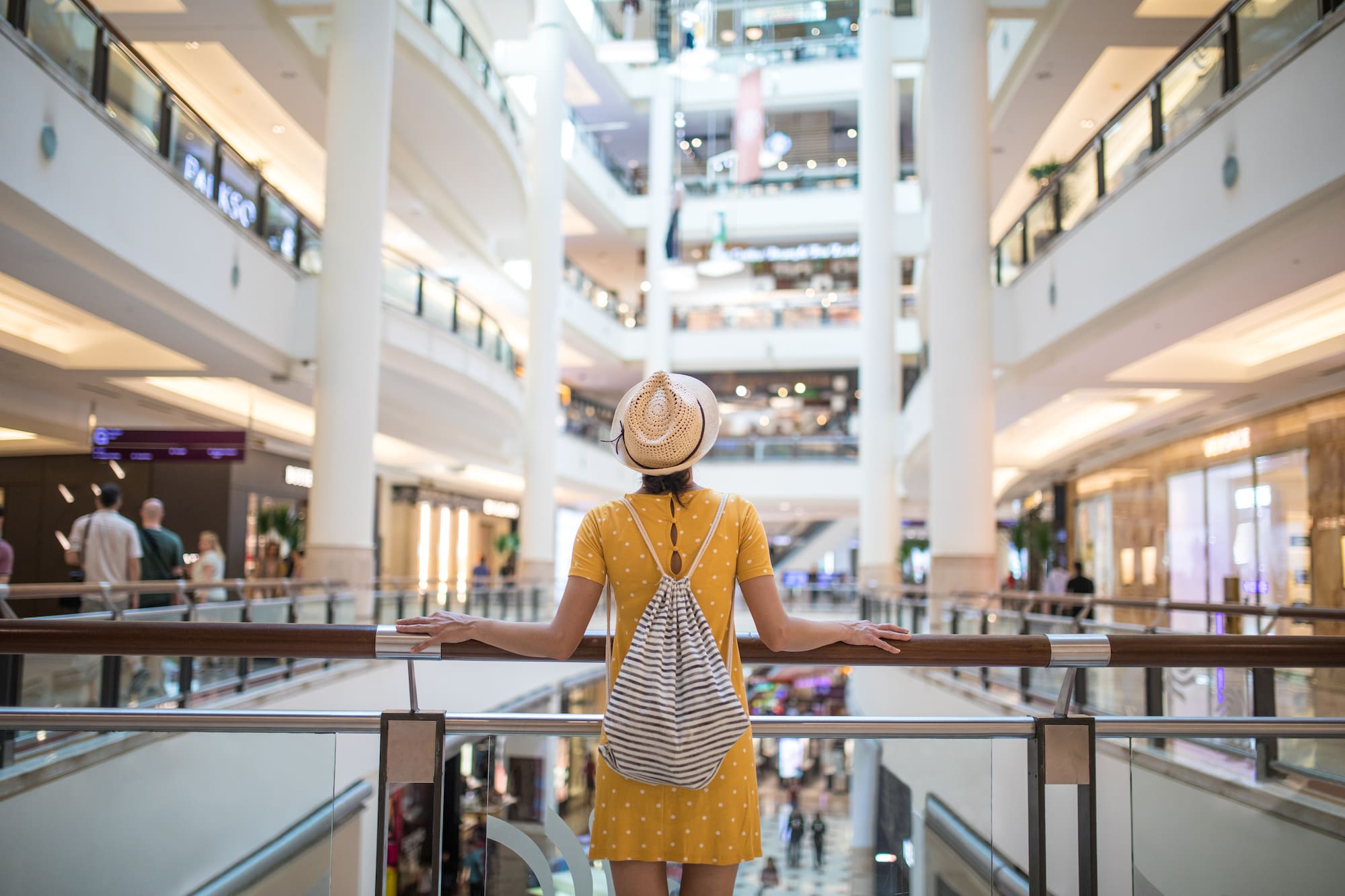 a woman in a yellow dress and hat standing by a railing in a large building