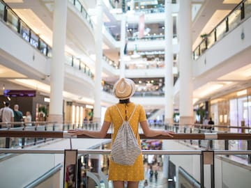 A woman in a yellow dress and hat stands beside a railing in a spacious building.