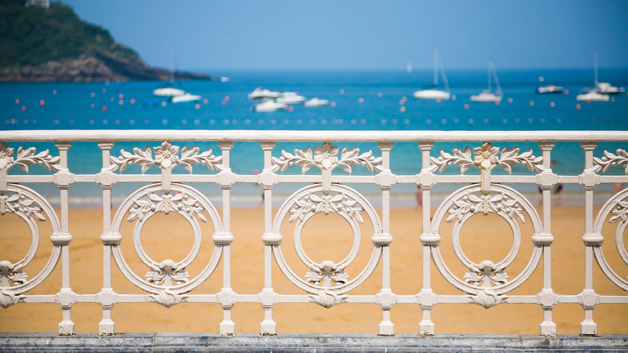 a white fence with a beach and boats in the background