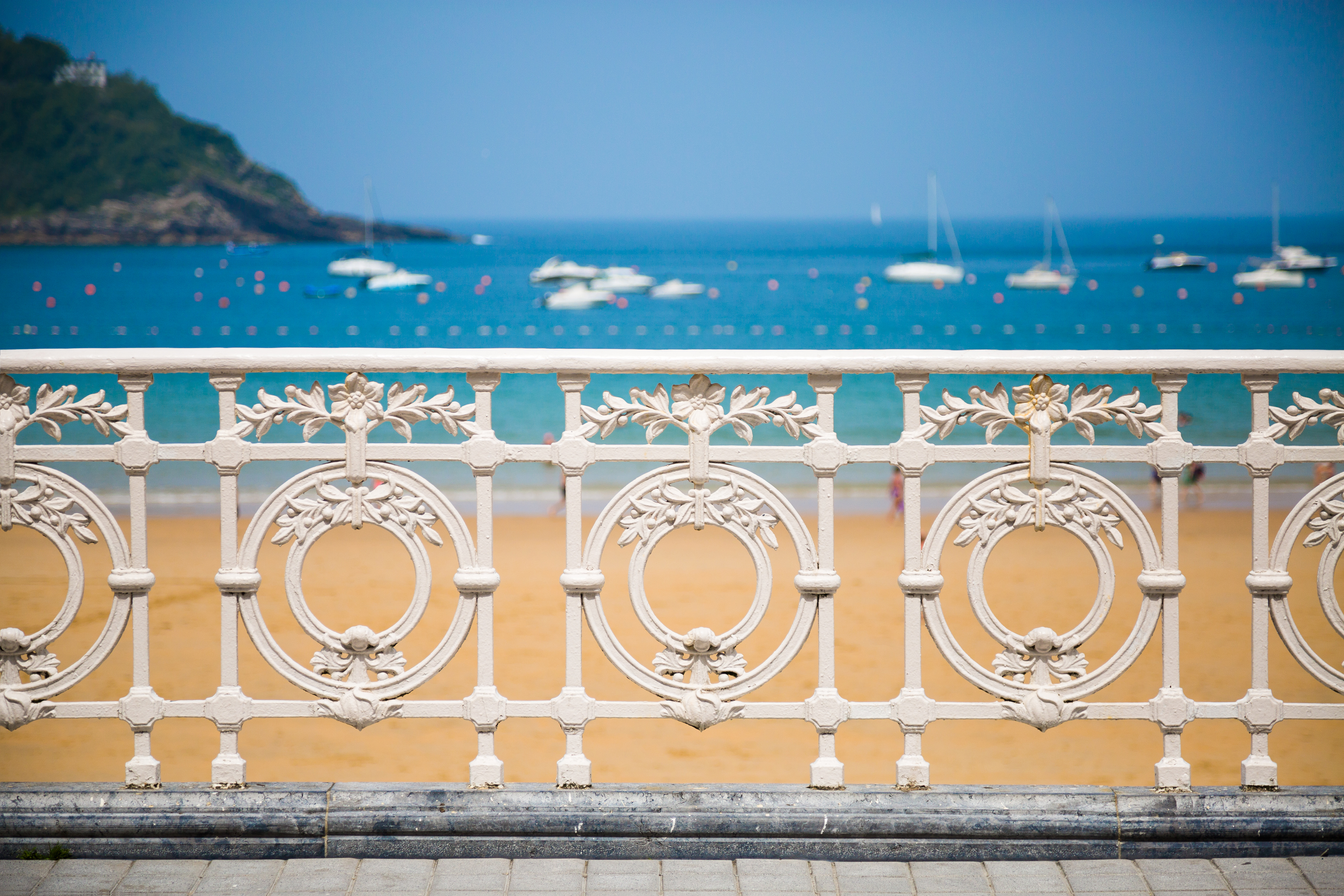 a white fence with a beach and boats in the background