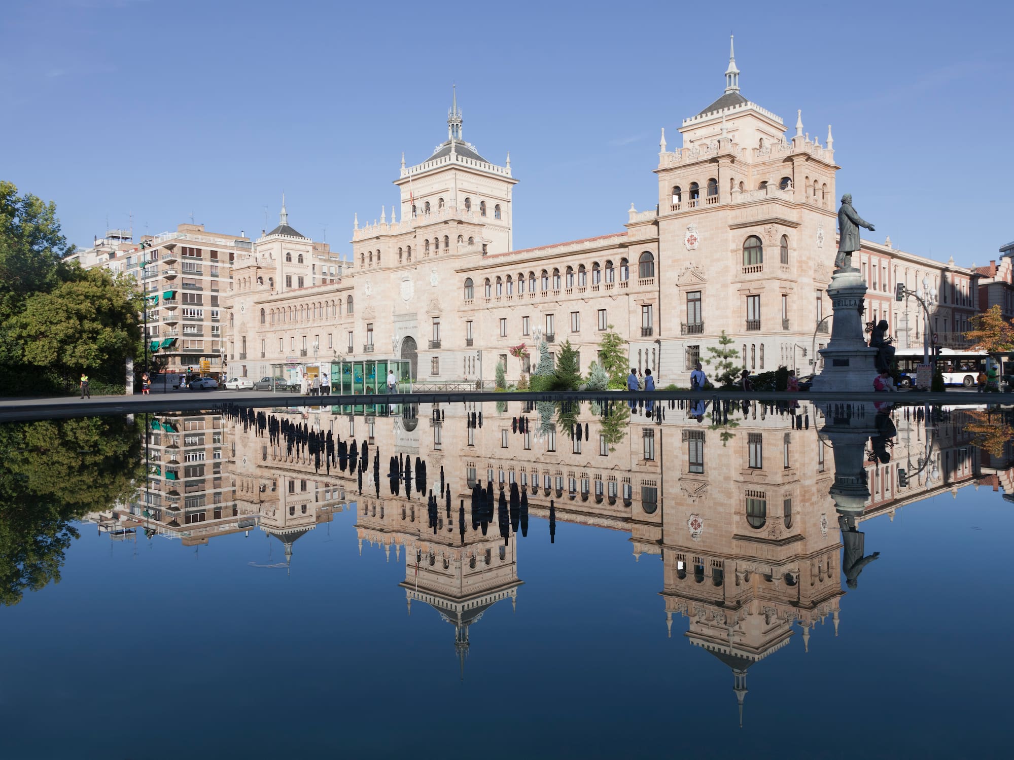 Ornate stone building with towers reflected in plaza water, Valladolid, Spain.