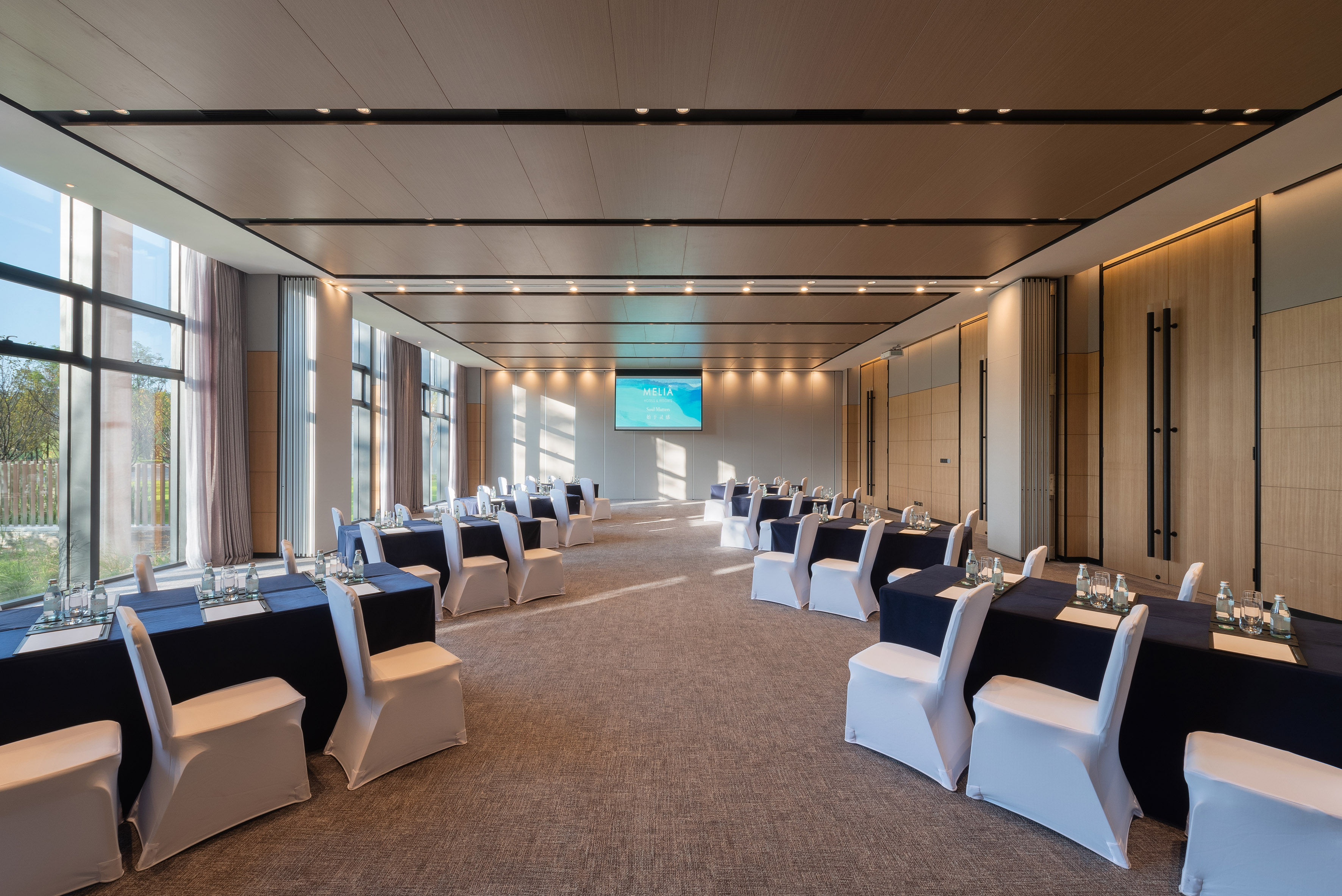 Modern Meliá conference room with U-shaped tables, white chairs, and projector.