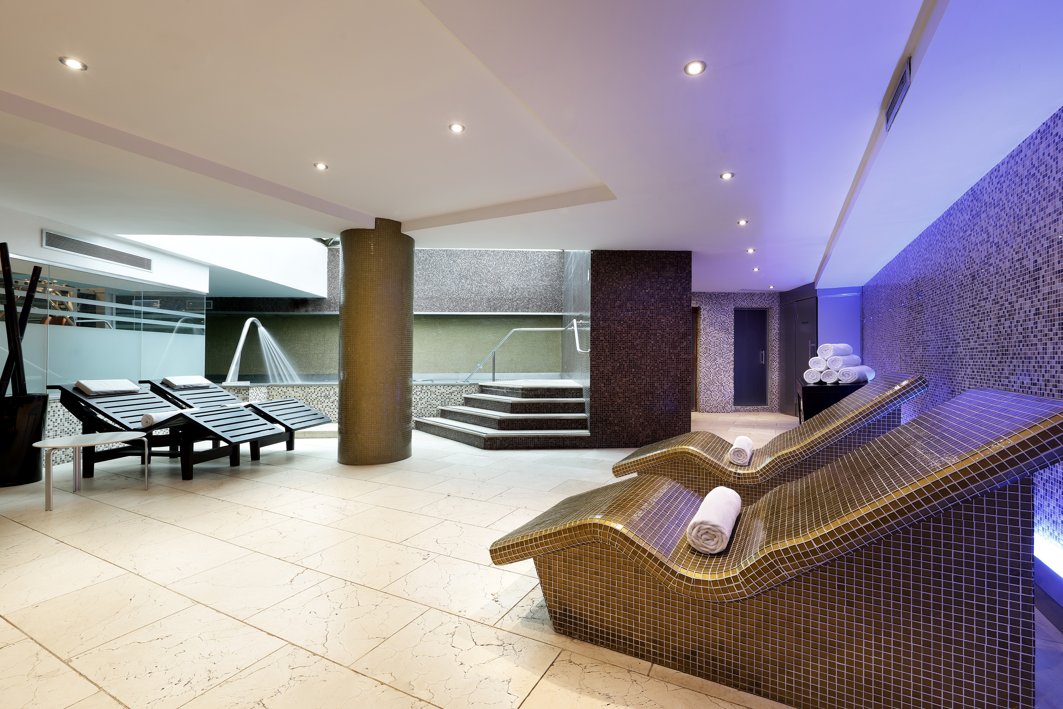 Luxury thermal spa with mosaic loungers, heated pool, and ambient lighting.