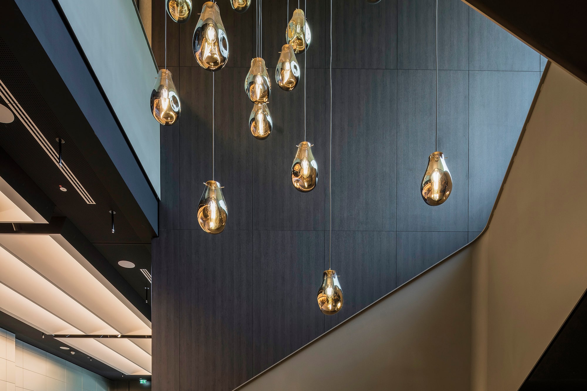 Contemporary lobby staircase with golden teardrop pendant lights.