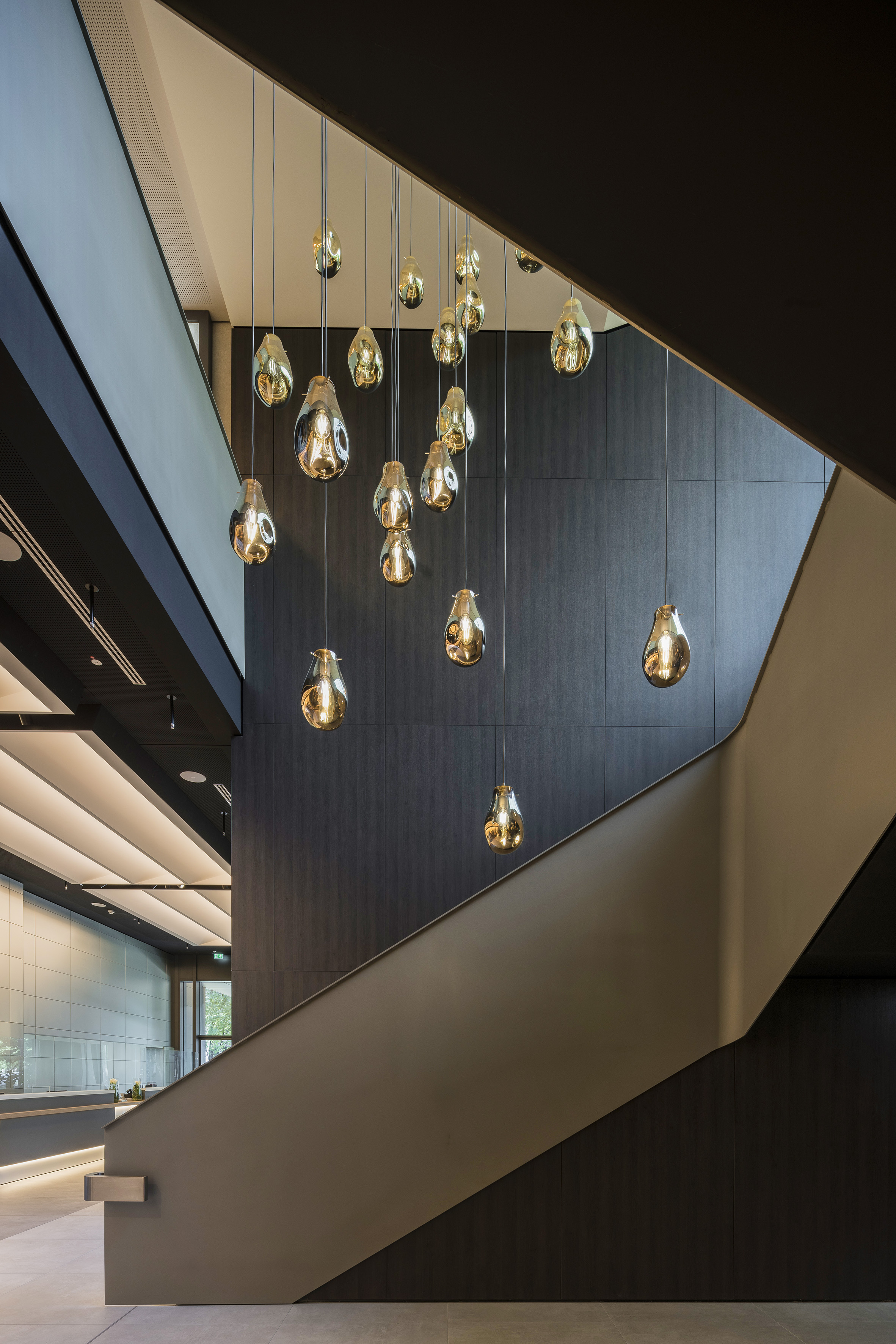Contemporary lobby staircase with golden teardrop pendant lights.