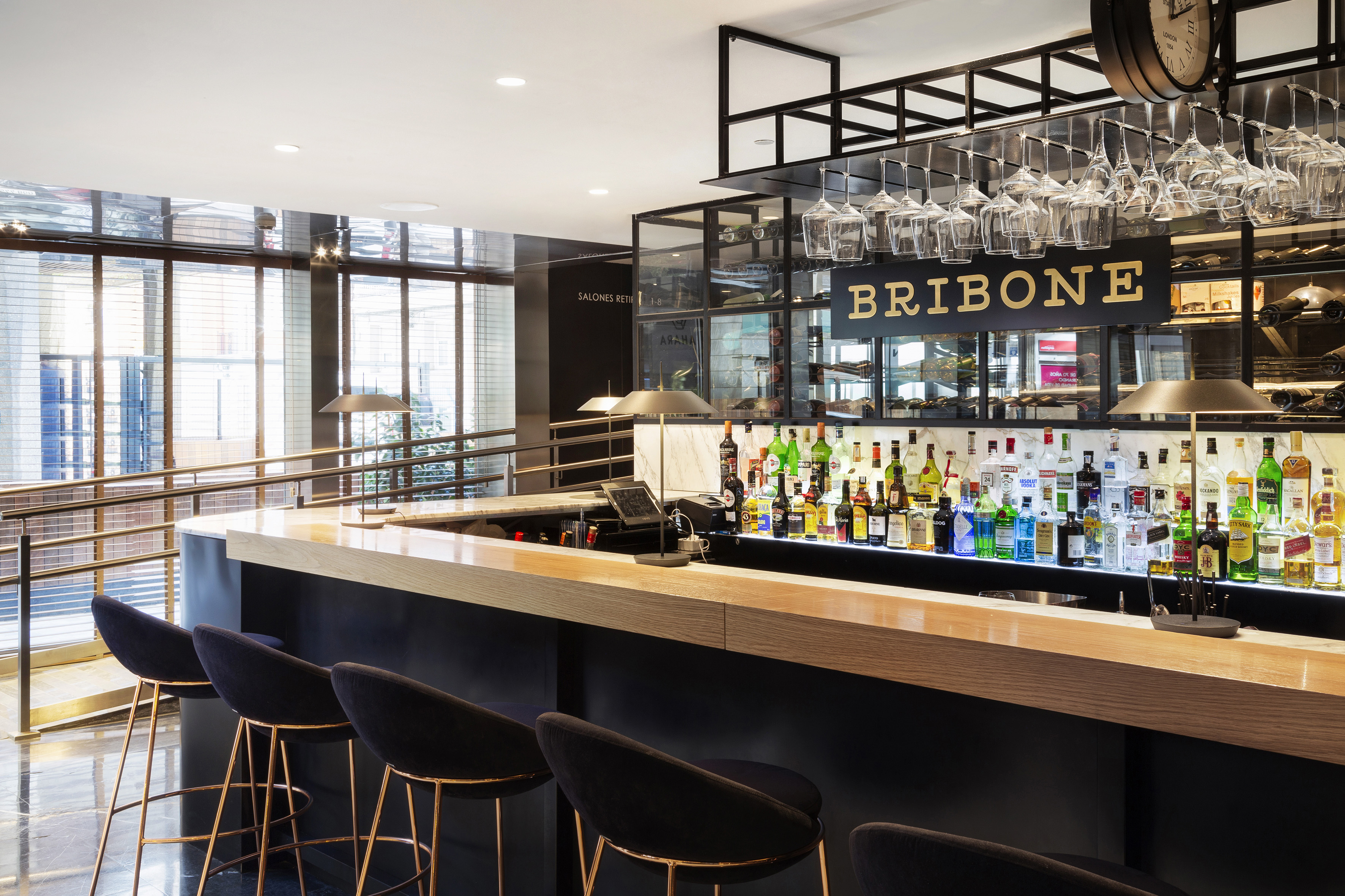 Modern hotel bar with BRIBONE sign, backlit liquor display, and black stools.