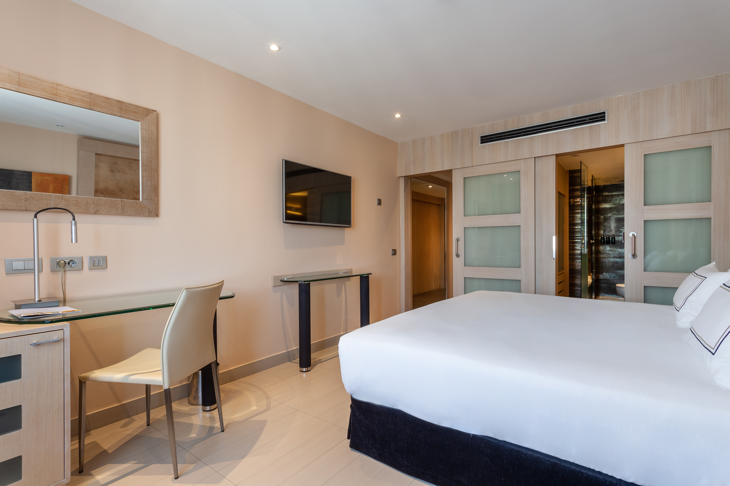 Modern hotel room with bed, desk, wall-mounted TV, and sliding bathroom doors.