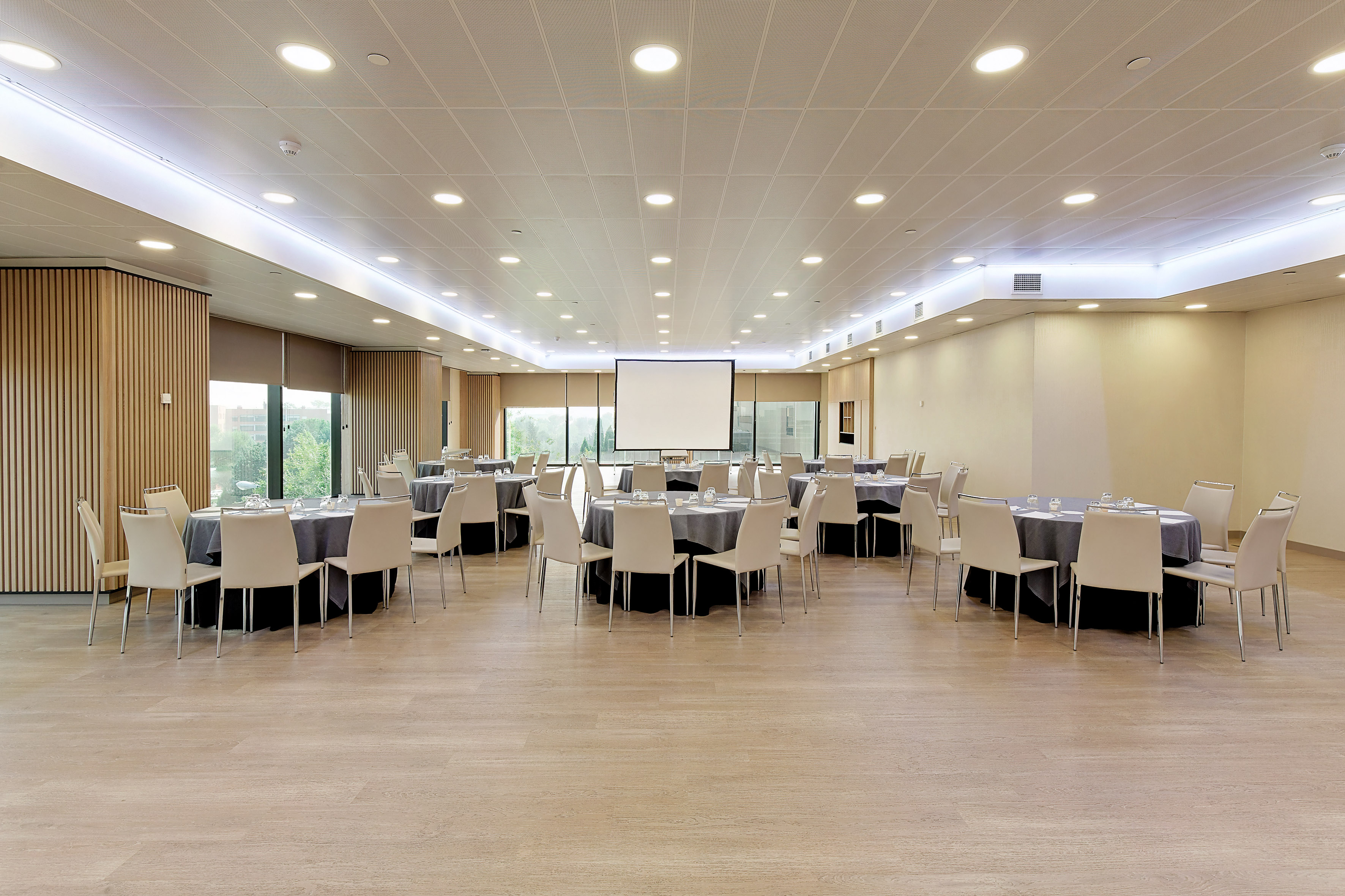 Modern meeting and event room with round tables, chairs, projector screen.