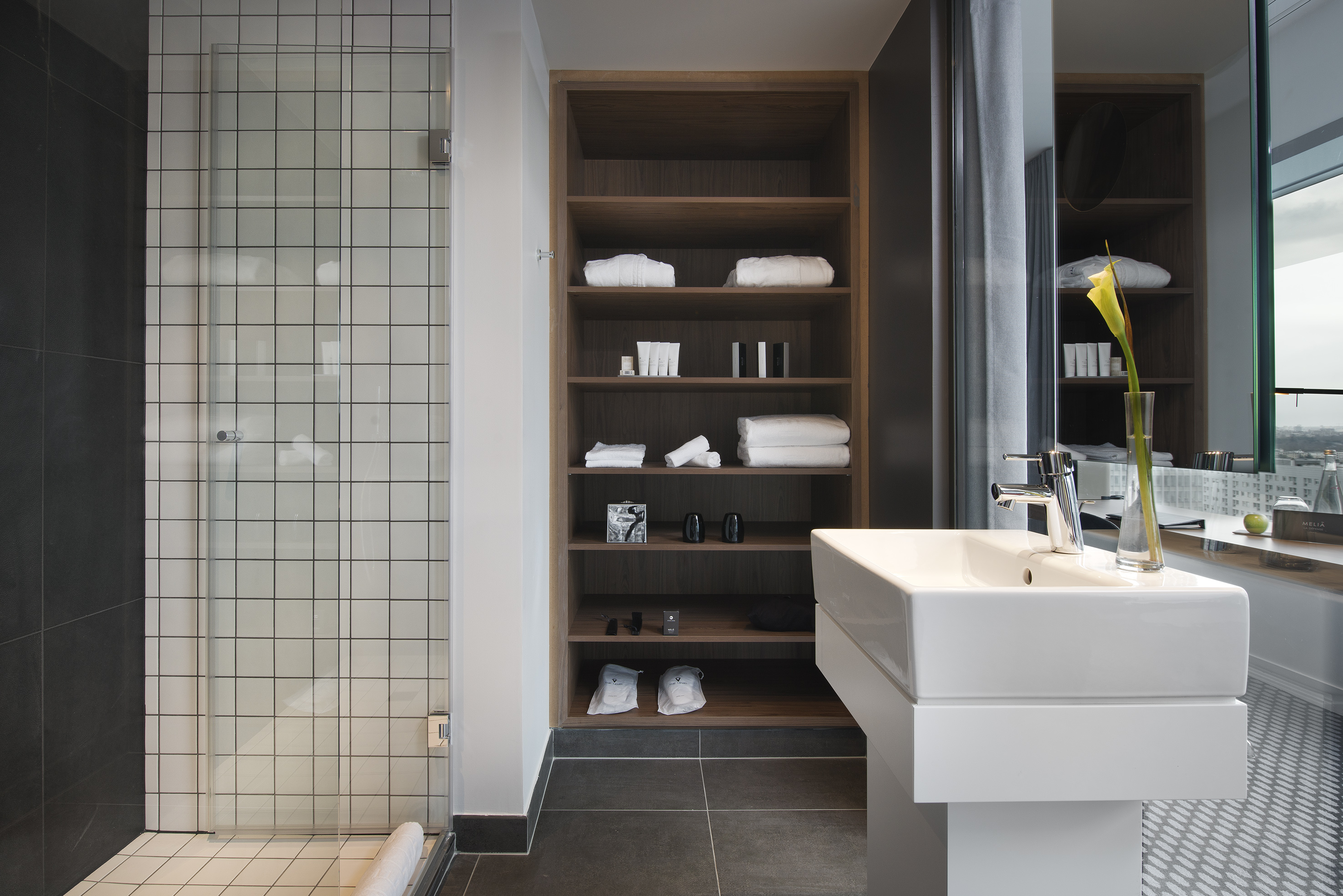 Modern bathroom with tiled shower, wooden shelves, white sink, and hotel amenities.